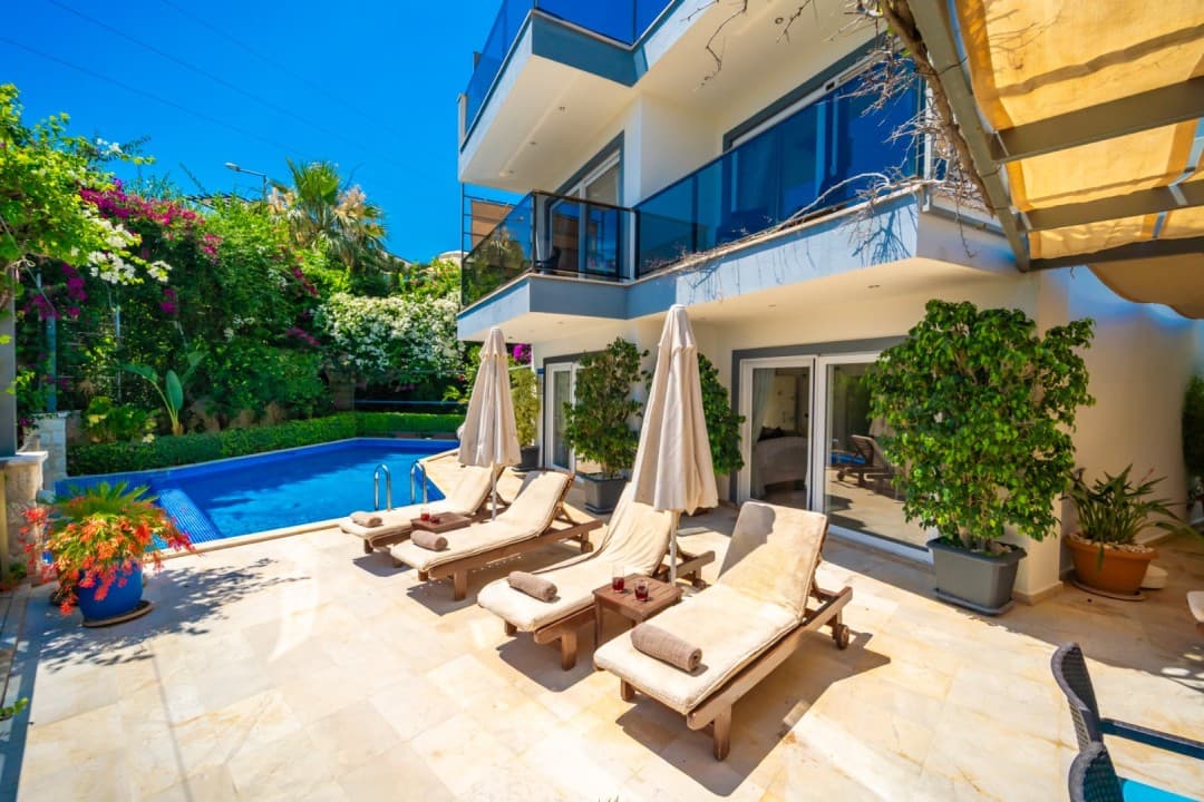 Havuz kenarında şezlonglar ve yeşillikler içindeki villa.