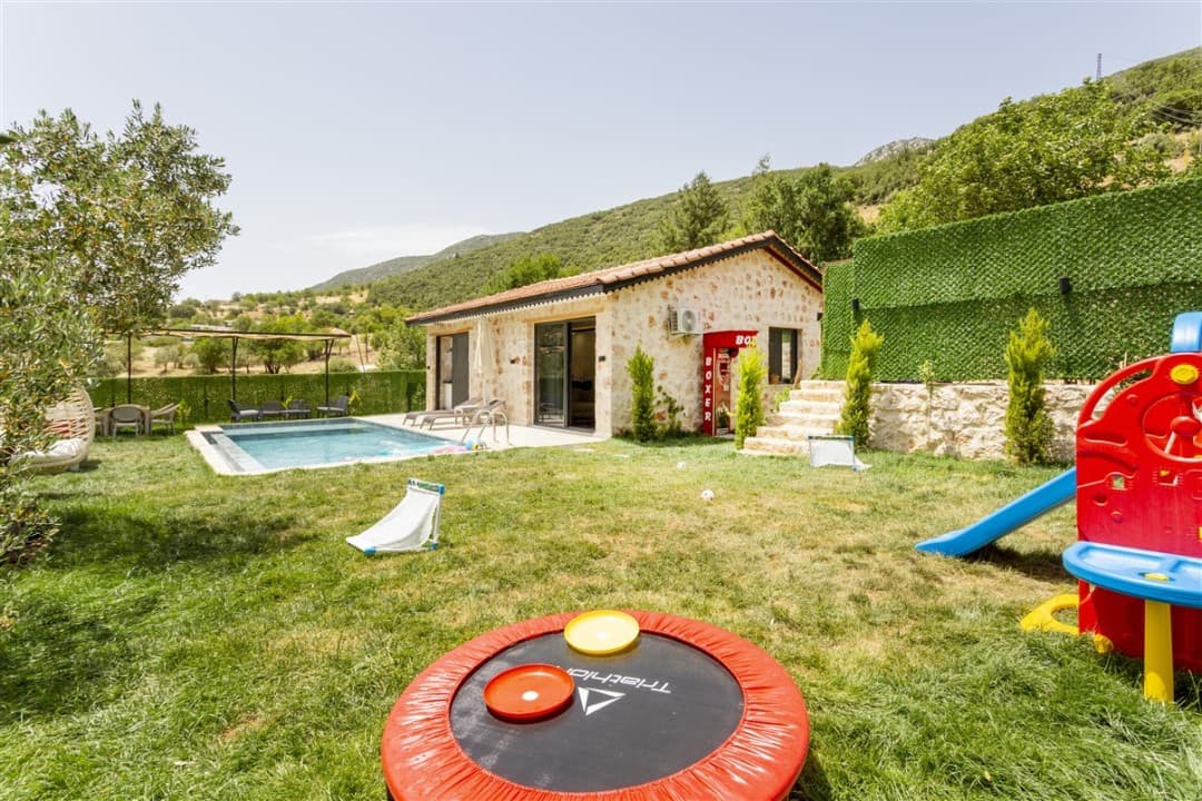 Taş duvarlı tek katlı villa, bahçesinde yüzme havuzu, çocuk oyun alanı, trambolin ve boks makinesi bulunuyor.