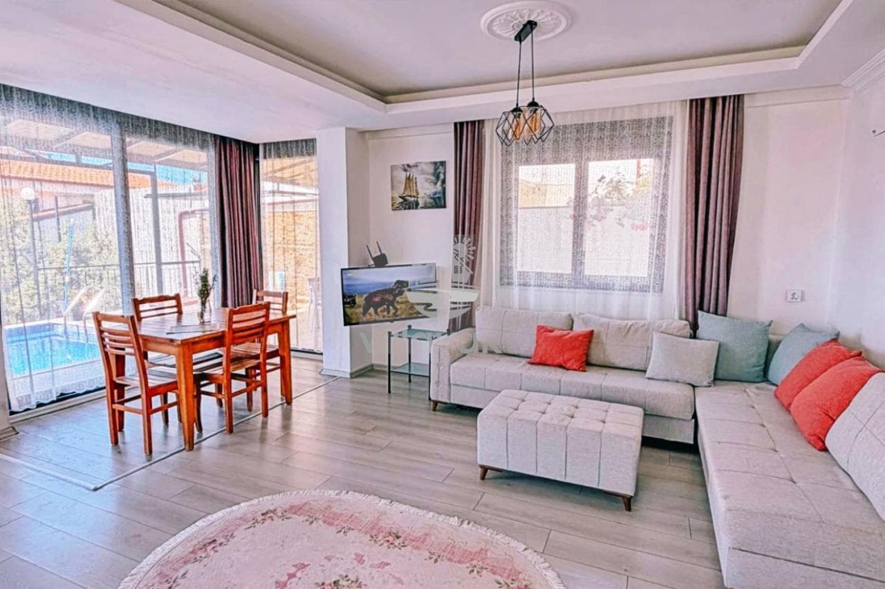 Gri L koltuk, ahşap yemek masası ve televizyon bulunan aydınlık salon.