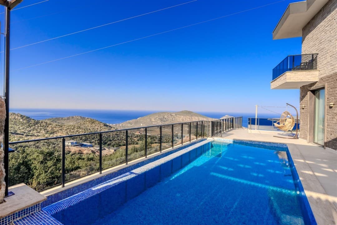 Balkonlu modern villanın önünde deniz ve dağ manzaralı sonsuzluk havuzu bulunuyor.