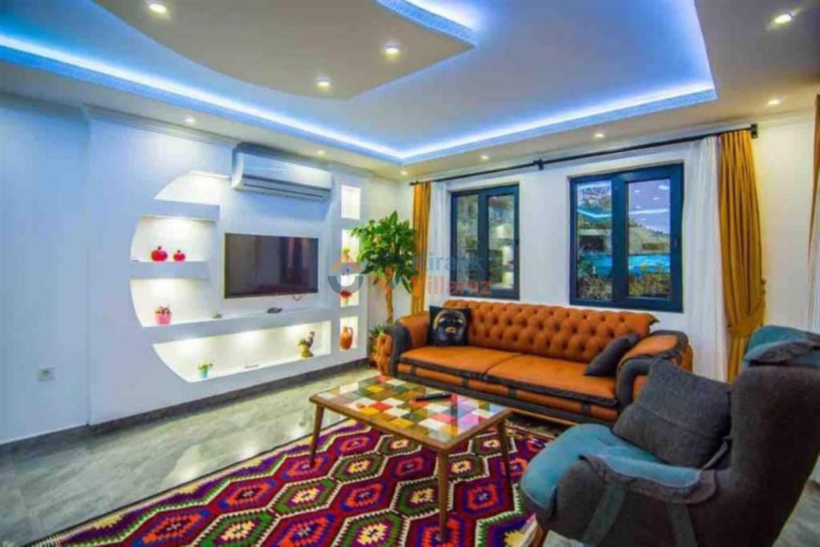 Renkli halılı, turuncu koltuklu ve TV üniteli oturma odası.