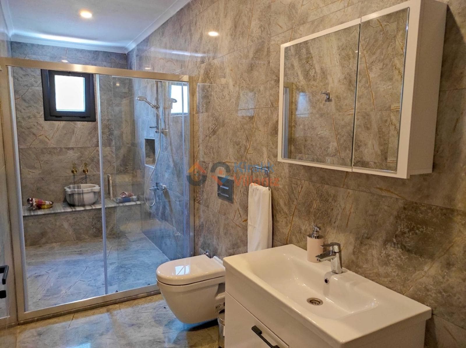 Gri mermer kaplı banyoda duşakabin, lavabo ve klozet yer alıyor.
