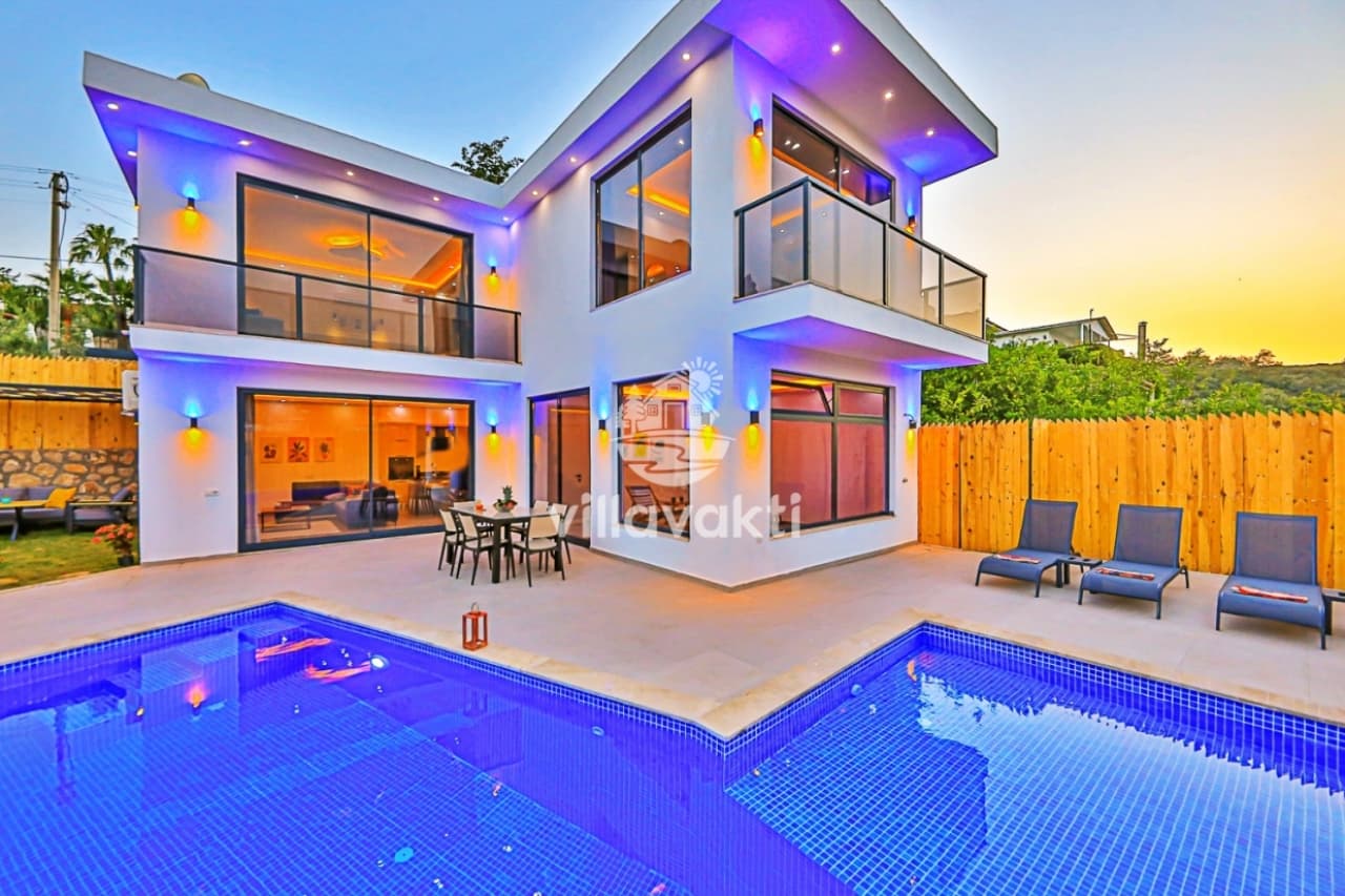 Önünde özel havuz ve şezlonglar bulunan, akşam ışıklandırmalı modern beyaz villa dış cephesi.