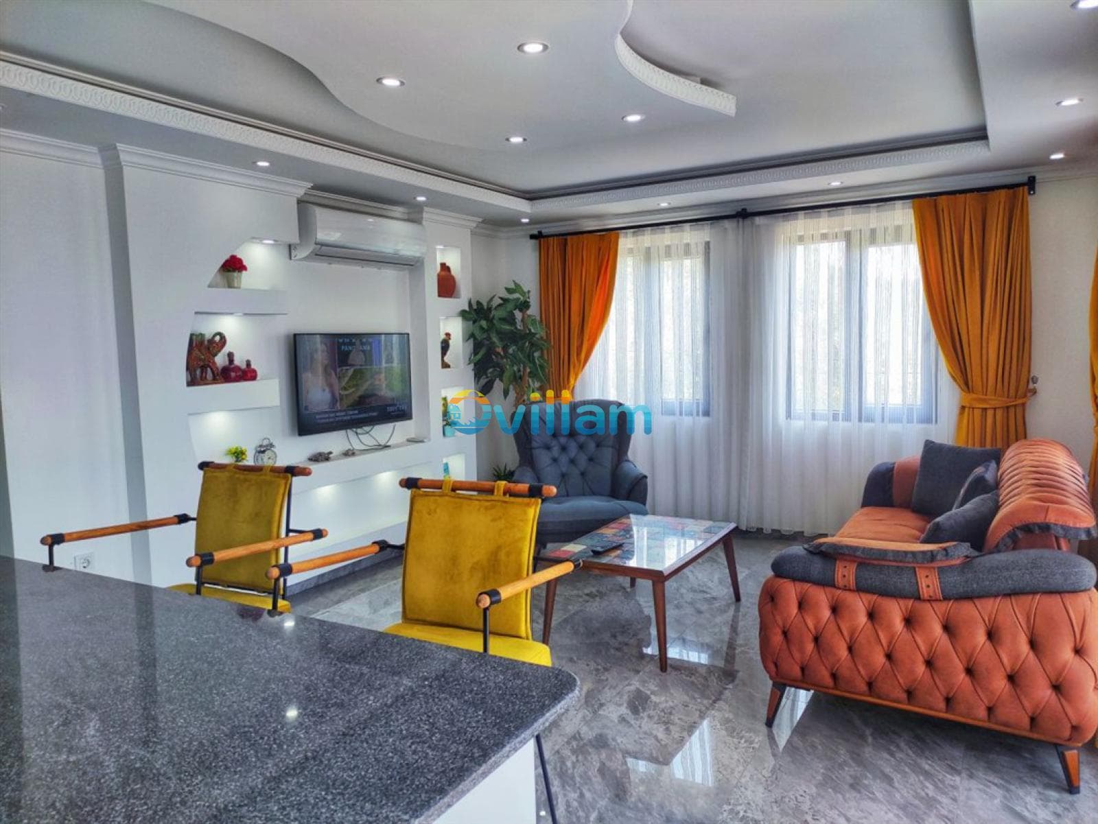 Turuncu perdeli ve gri koltuklu modern salon ve mutfak tezgahı.
