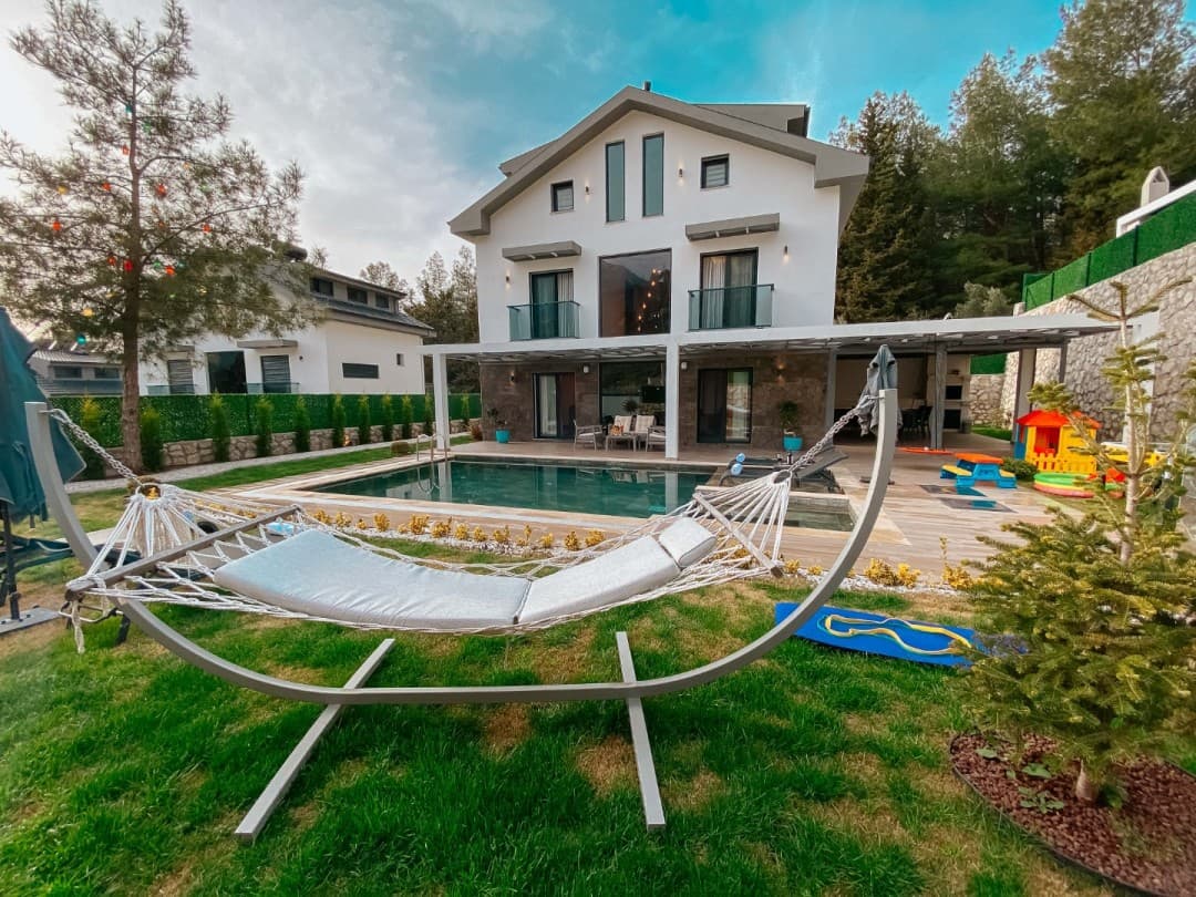 Ön planda salıncak olan, havuzlu ve bahçeli beyaz villa.