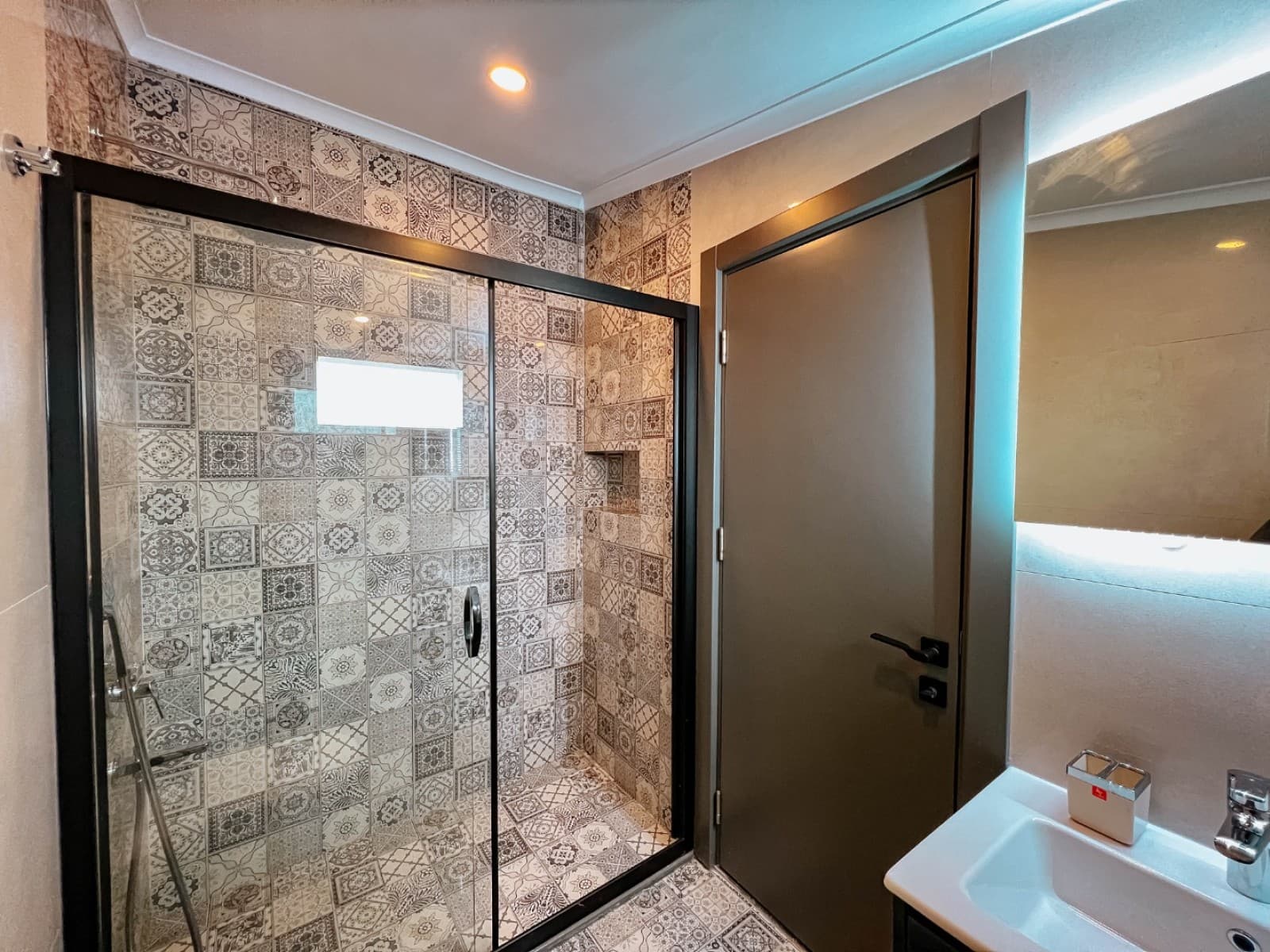 Desenli duvar karolarına sahip cam duşakabinli banyo ve lavabo alanı.