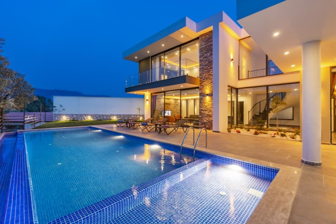 Akşam vakti havuzu ve ışıklandırılmış modern villanın dış görünümü.