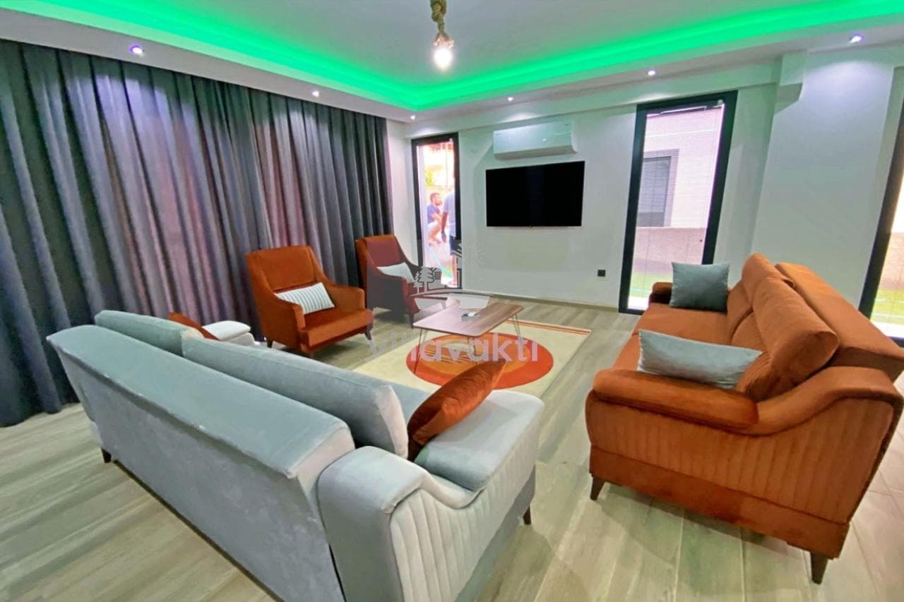 Yeşil ışıklandırmalı tavanı olan, gri ve turuncu koltuklu salon