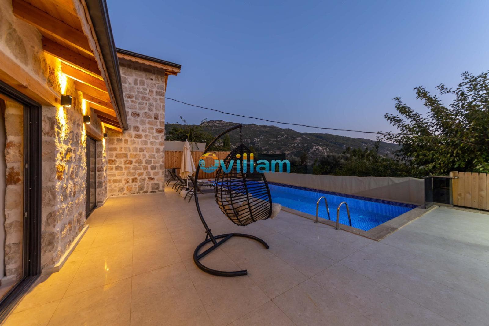 Salıncak ve havuzun bulunduğu taş duvarlı villa terası