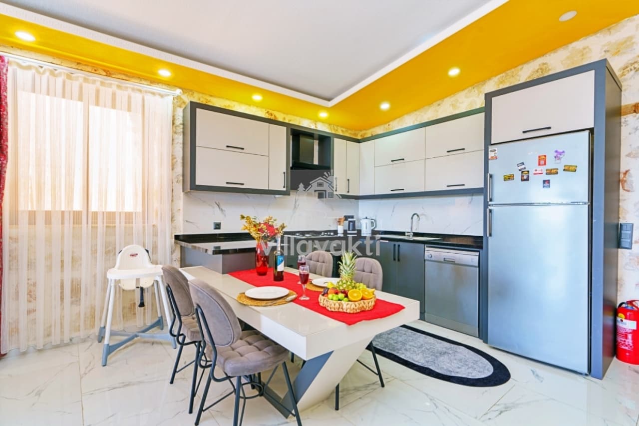 Gri dolaplı, beyaz tezgahlı ve ortada yemek masası olan modern mutfak.