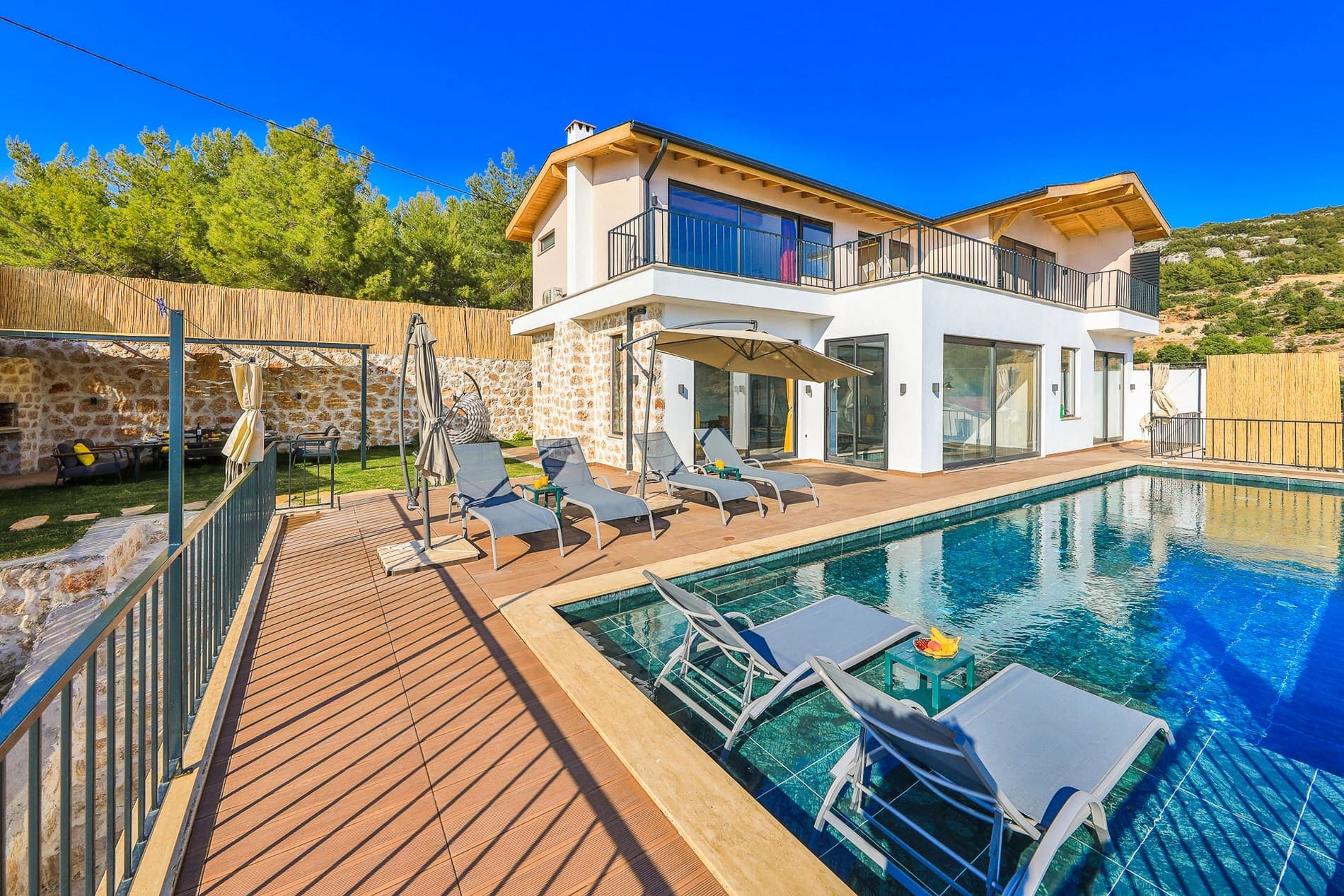 Ahşap korkuluklu balkonları olan iki katlı beyaz villa ve havuz.