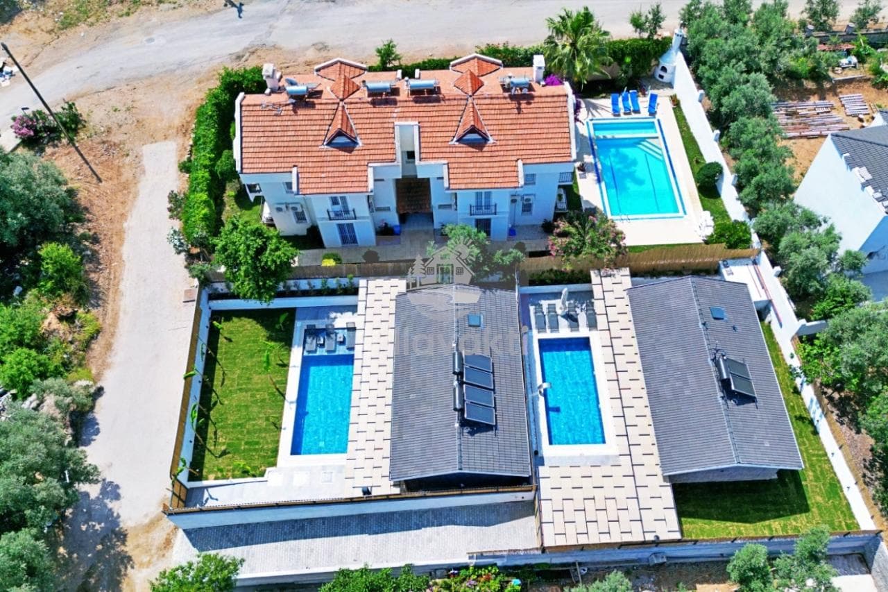 Kiremit çatılı iki katlı büyük villalar ve bahçesindeki yüzme havuzlarının havadan görünümü.