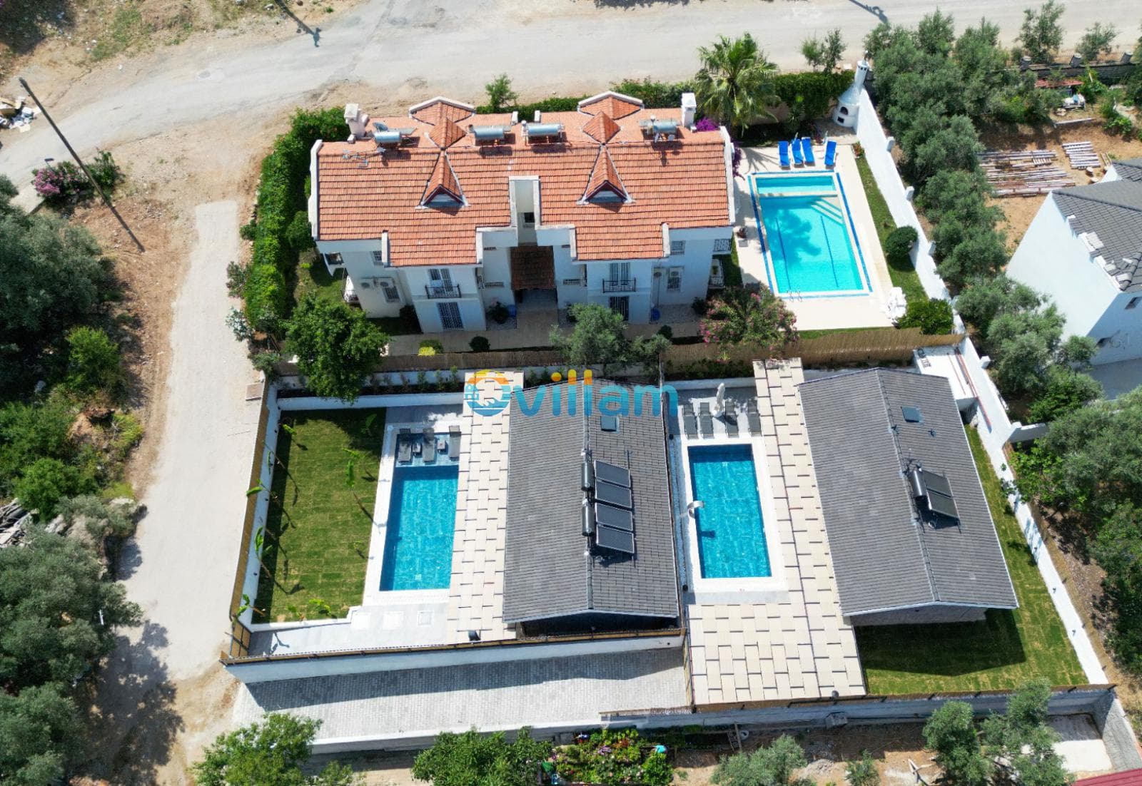 Kiremit çatılı beyaz villalar, havuzları ve geniş bahçesiyle yukarıdan görünüm.