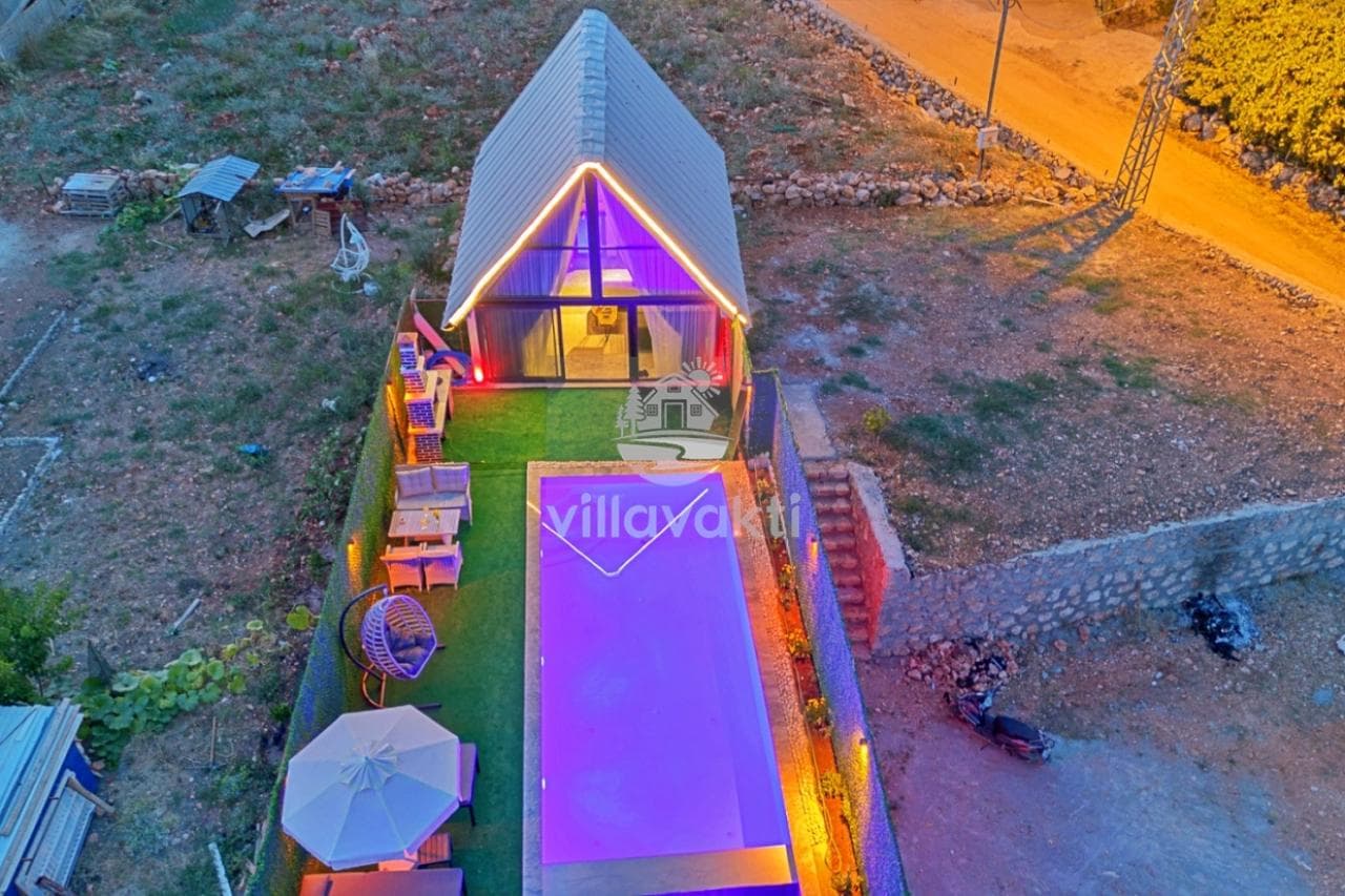 Üçgen çatıya sahip, aydınlatmalı modern villanın havuzlu bahçesinin kuşbakışı görünümü.