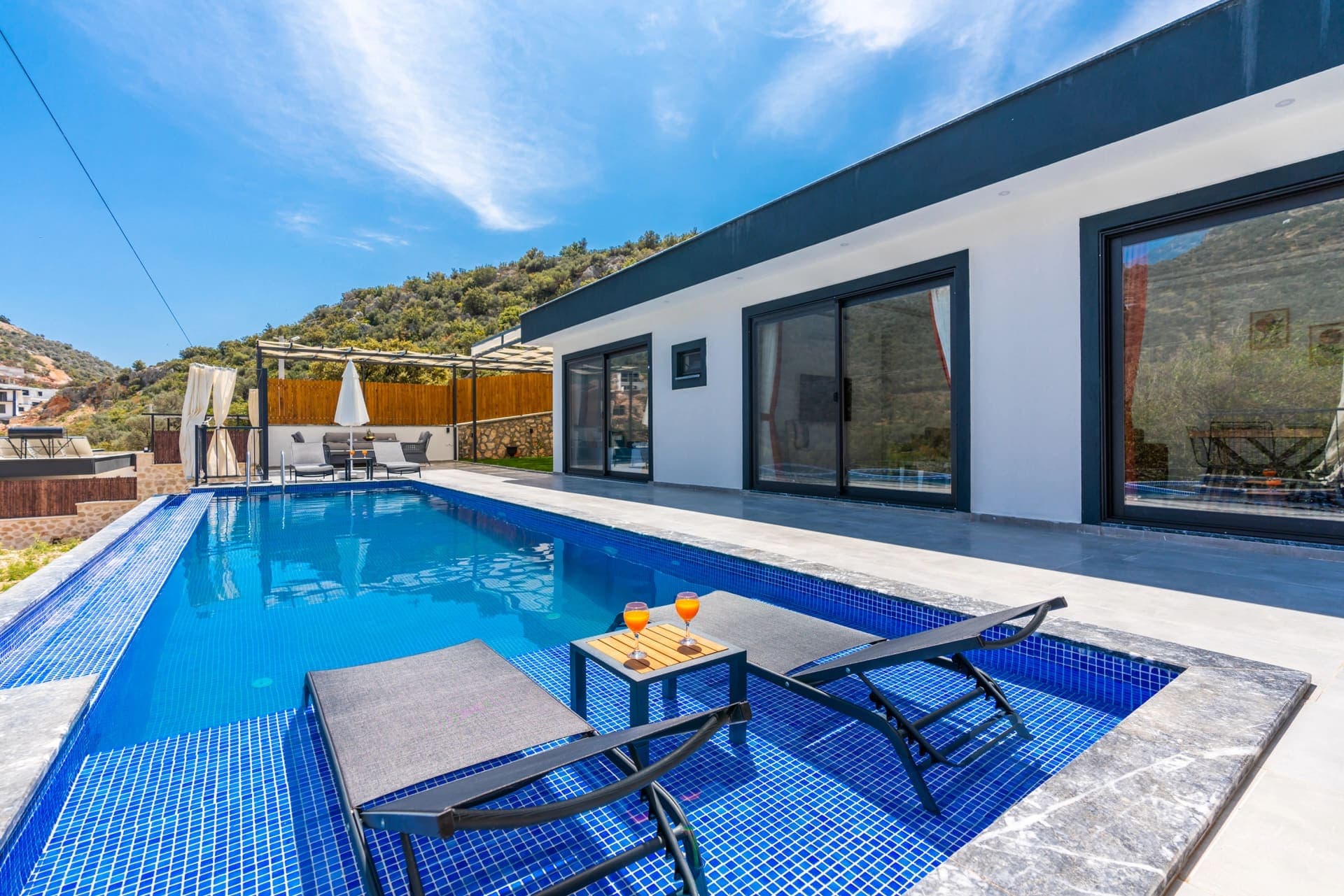 Mavi yüzme havuzu kenarında şezlonglar ve arka planda modern beyaz villa.