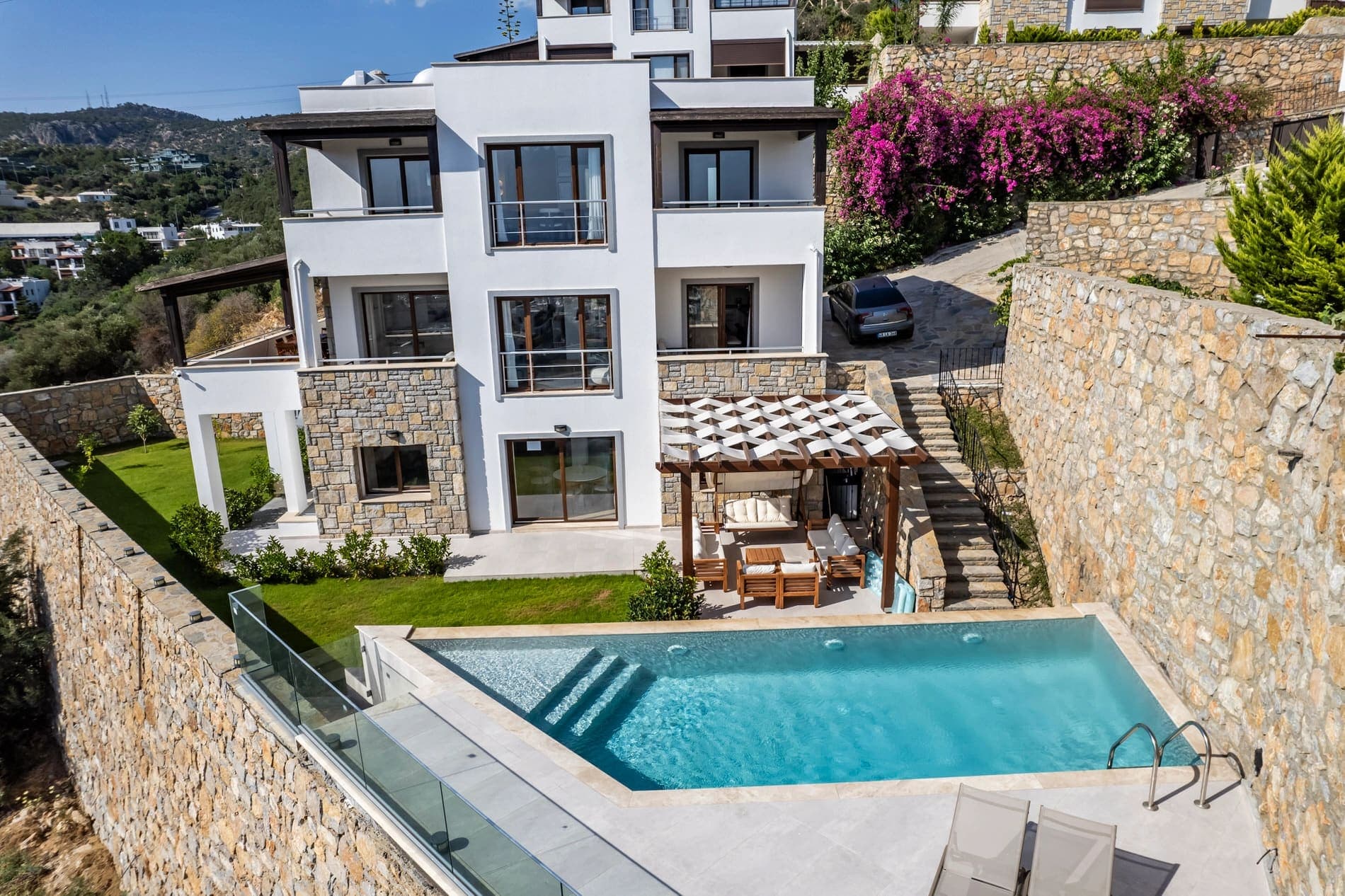 Taş detaylı beyaz dış cepheye sahip villa, yüzme havuzu ve bahçe alanı.