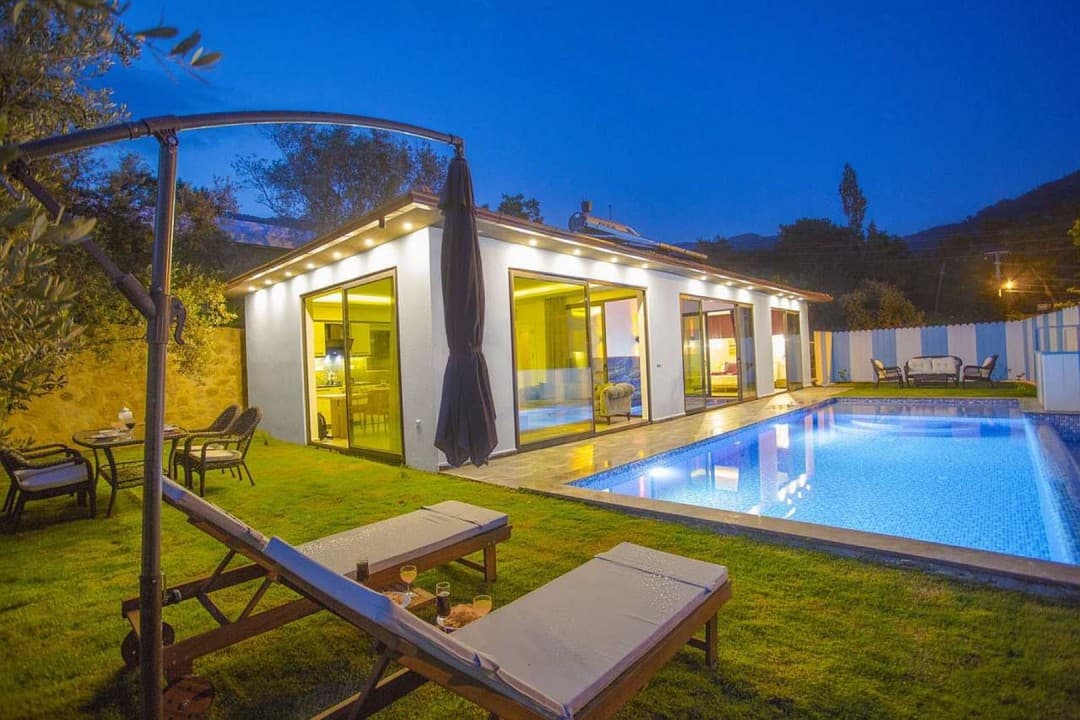 Akşam vakti aydınlatmalı havuzu ve şezlongları olan müstakil villa.
