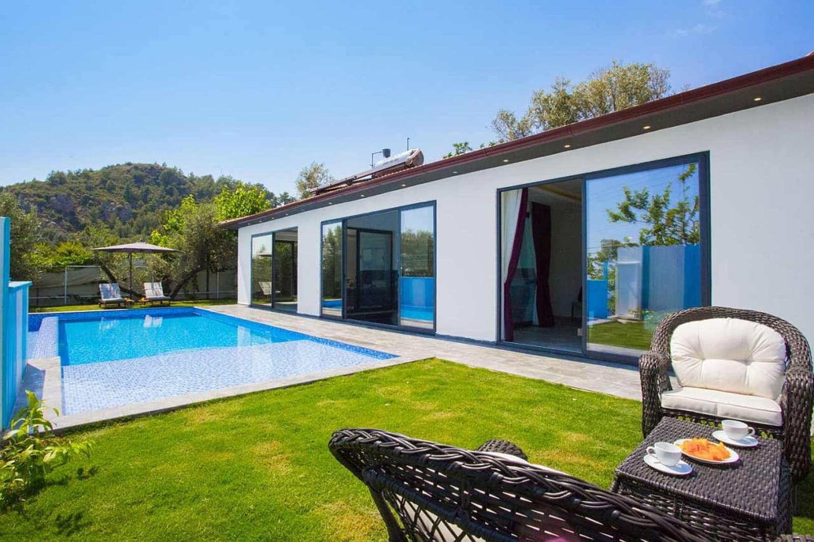 Mavi yüzme havuzu ve çim alanın bulunduğu villa bahçesi.