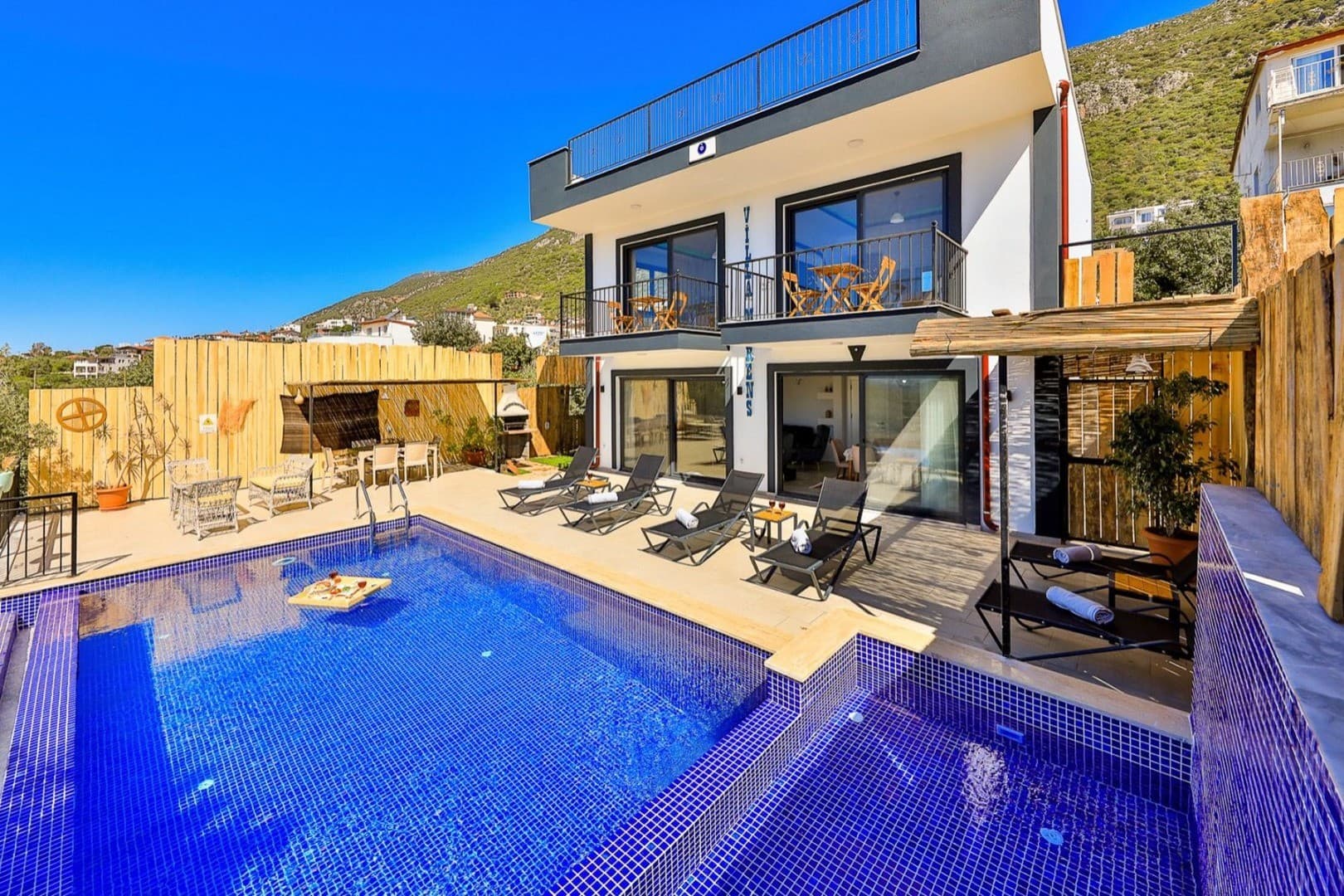 Mavi mozaik kaplı havuzu, şezlongları ve balkonları olan iki katlı Villa Morens 2 binası.