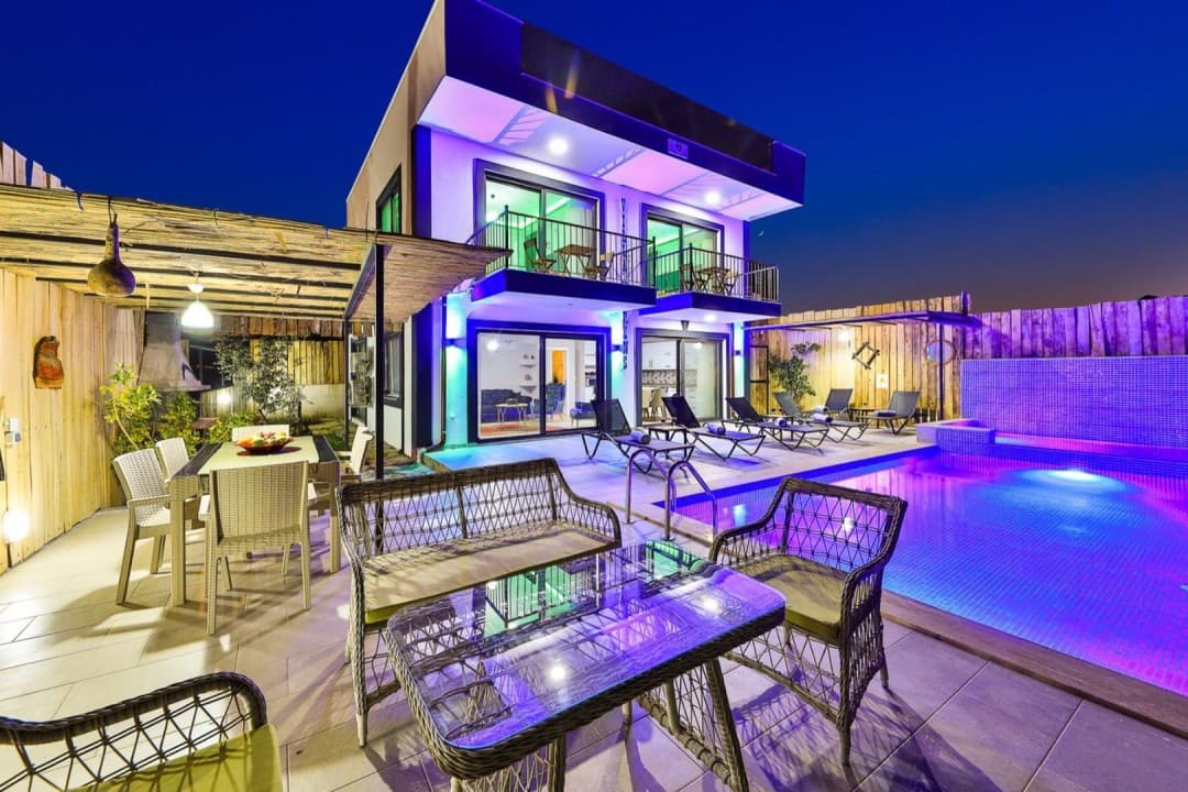 Akşam vakti havuz başı, şezlonglar ve aydınlatmalı iki katlı villa.