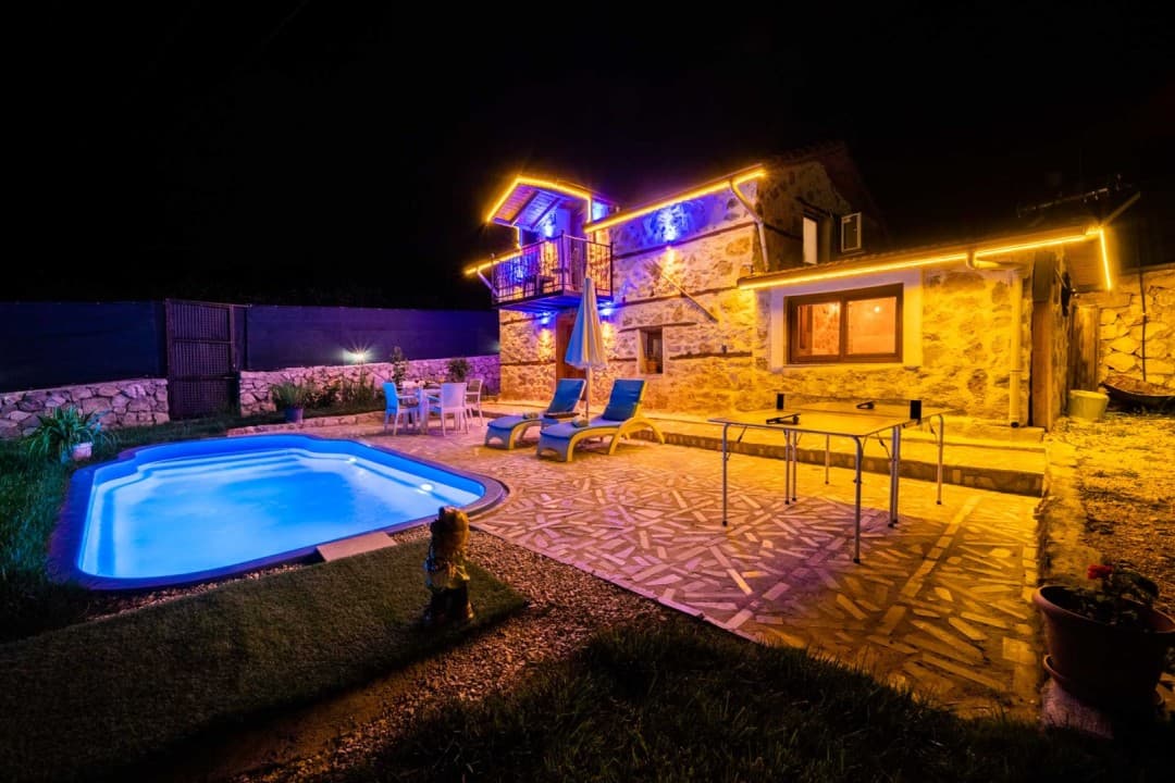 Gece aydınlatmalı taş villa ve önünde havuz, masa tenisi.