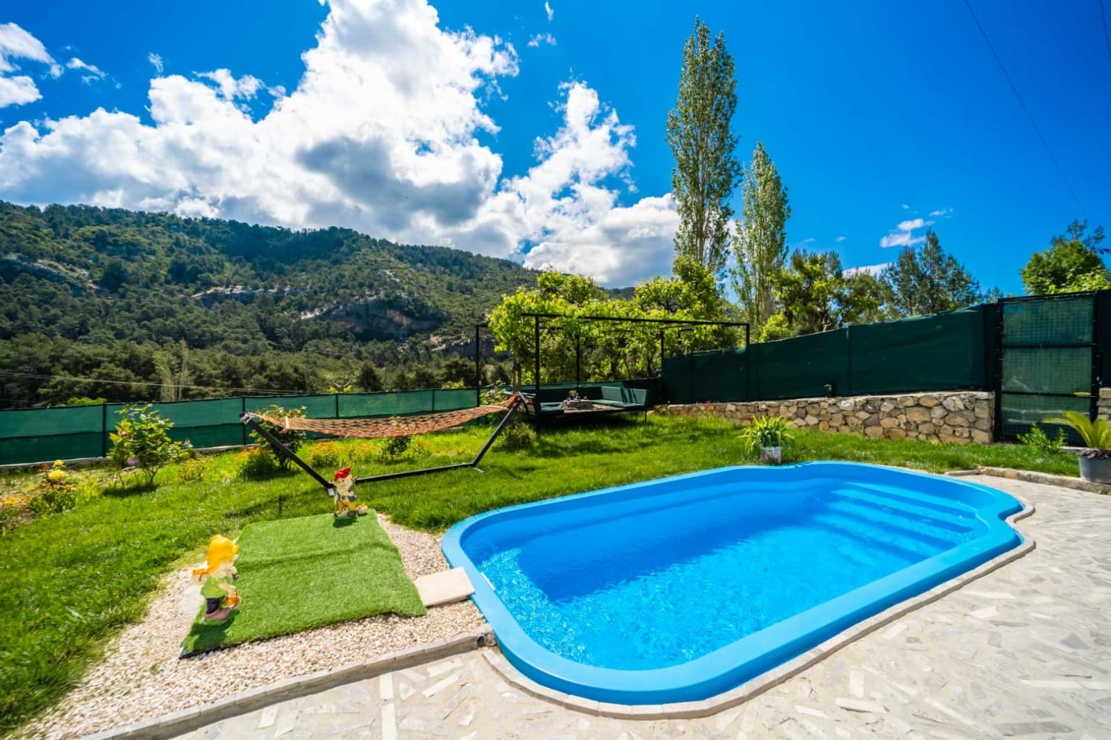 Bahçesinde hamak, mavi havuz ve yeşil dağ manzarası olan villa dış alanı.