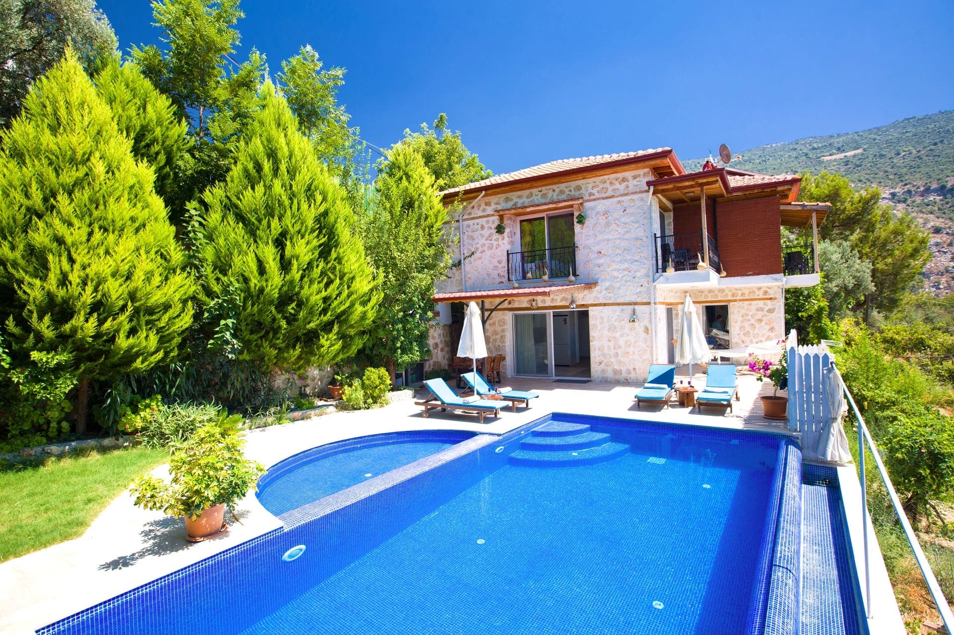 Bahçesinde havuz ve şezlonglar bulunan taş dış cepheli iki katlı villa.