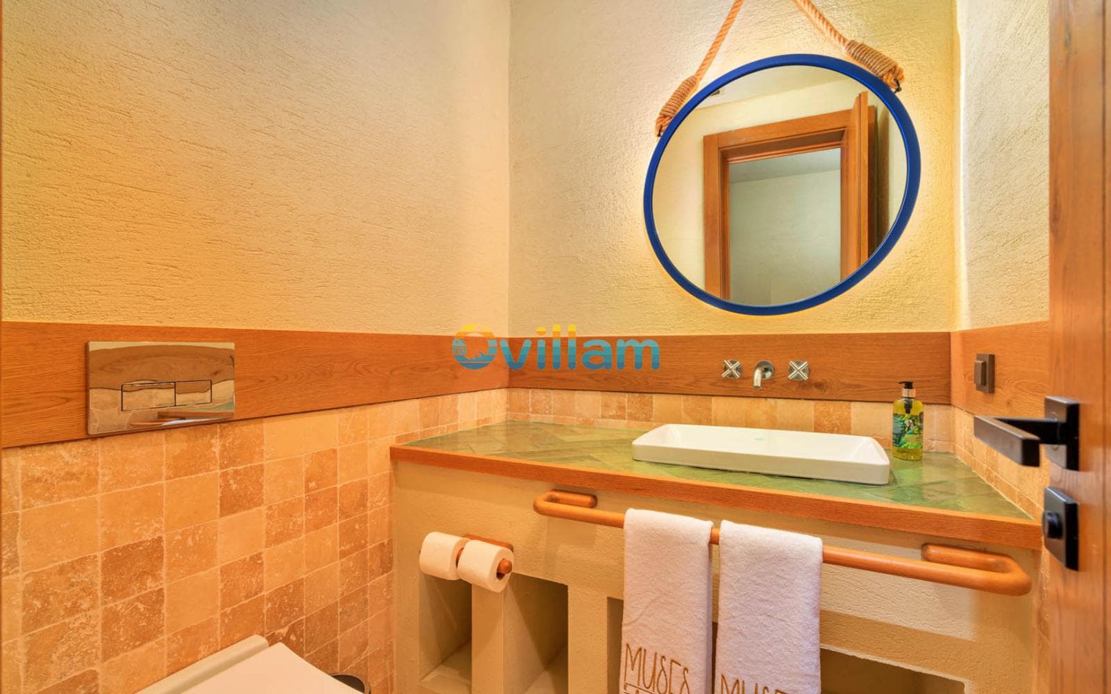 Bej tonlarında banyoda yuvarlak ayna ve ahşap detaylı lavabo.