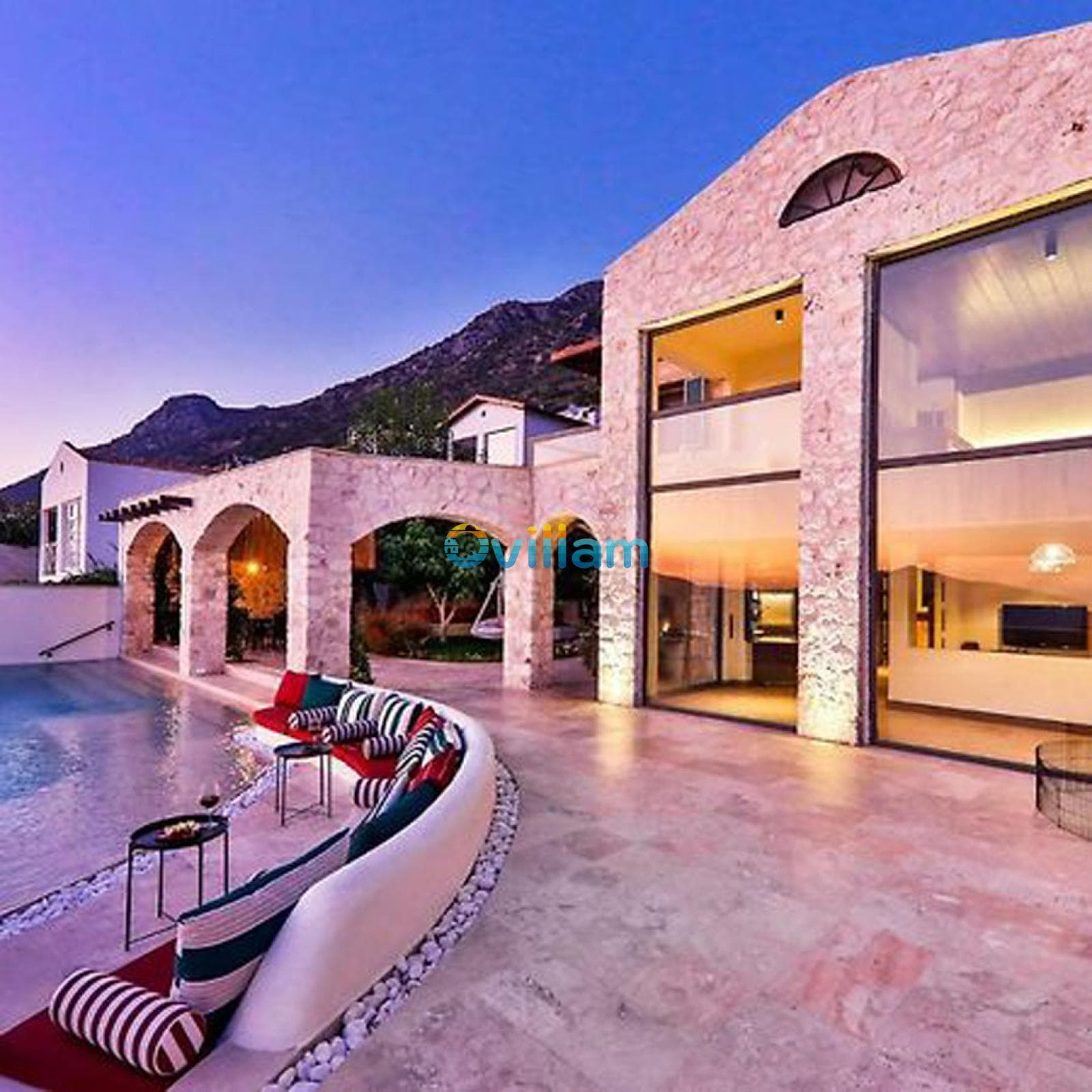 Akşam ışıklandırmalı taş villa ve havuz başı oturma alanı.