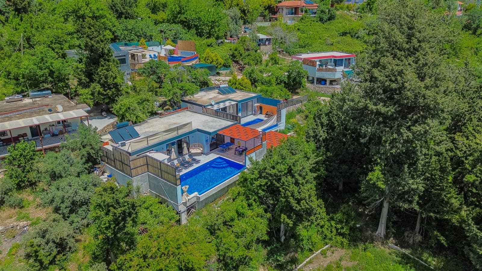 Yeşillikler içinde, havuzlu ve teraslı villanın havadan görünümü.