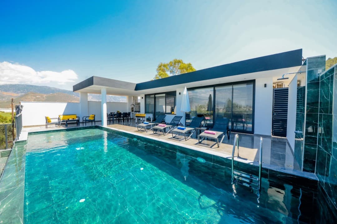Mavi havuzlu, şezlonglu, veranda alanında yemek masası bulunan modern tek katlı villa.