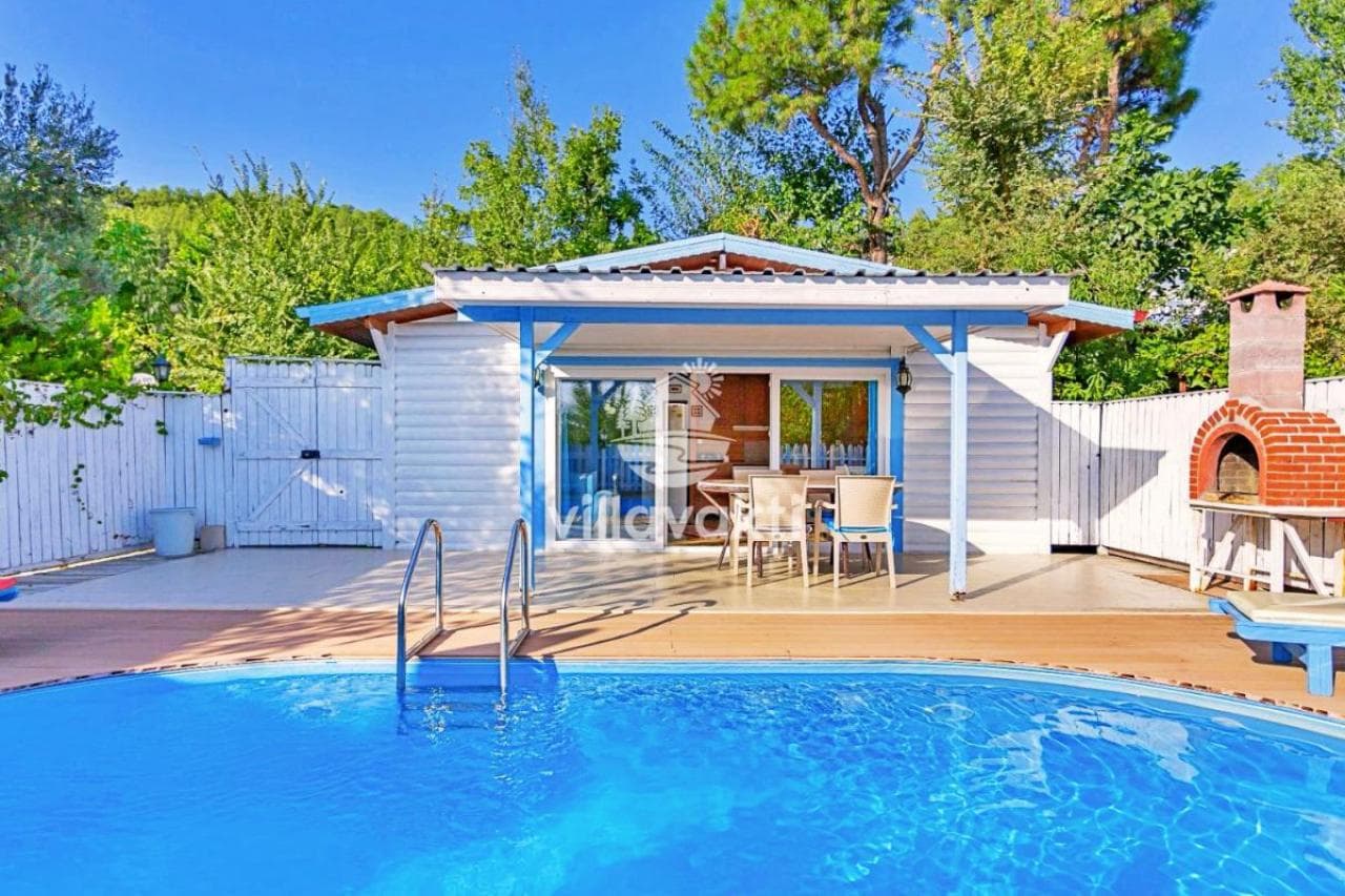 Bahçesinde havuz ve önünde yemek masası bulunan tek katlı beyaz villa.