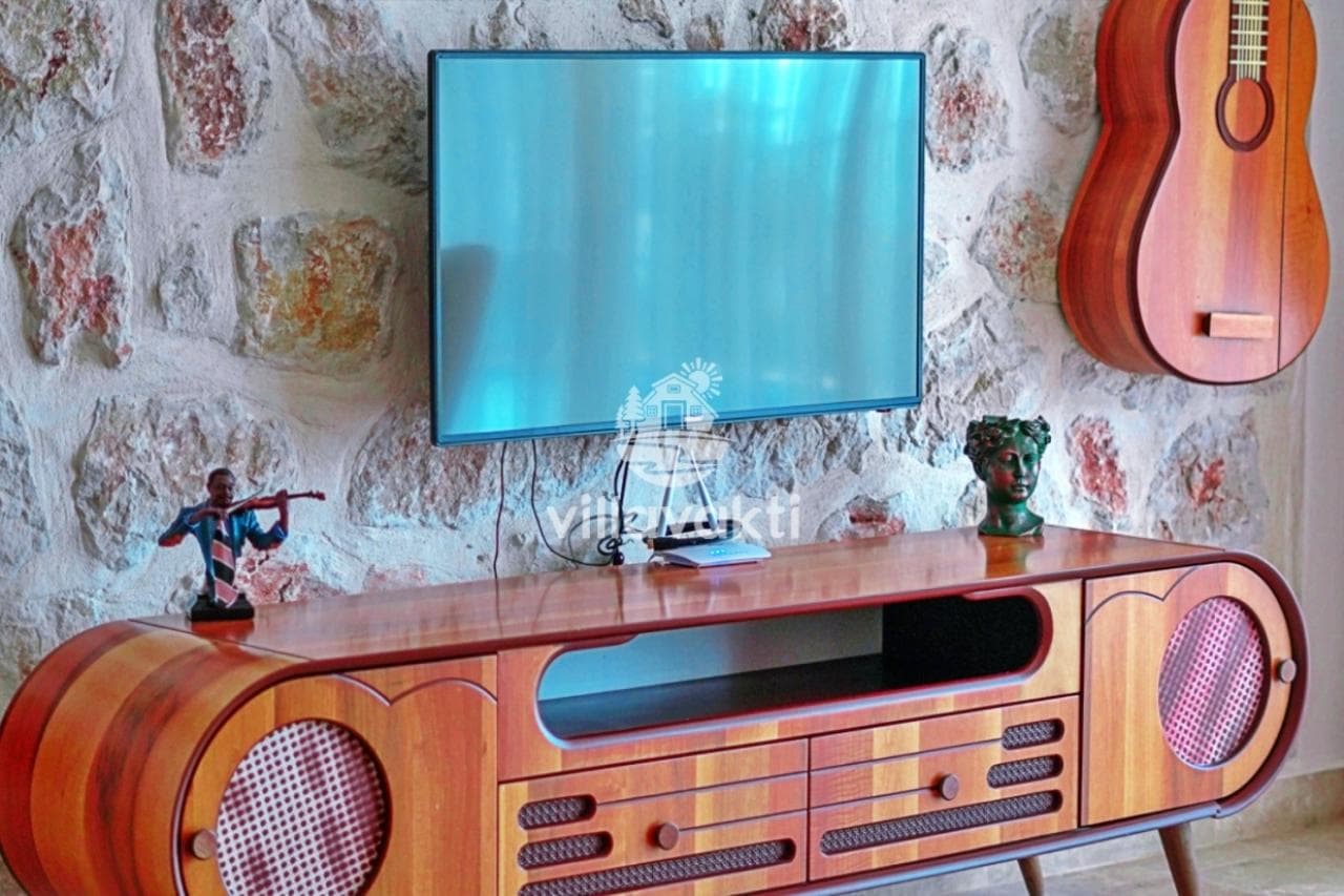 Ahşap TV ünitesi ve duvarda asılı dekoratif gitar bulunan iç mekan.