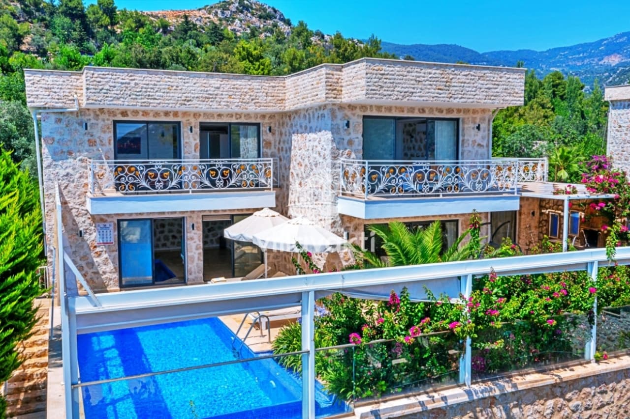 Taş cepheli, balkonlu ve havuzlu iki katlı villa ve çevresindeki yeşil doğa.