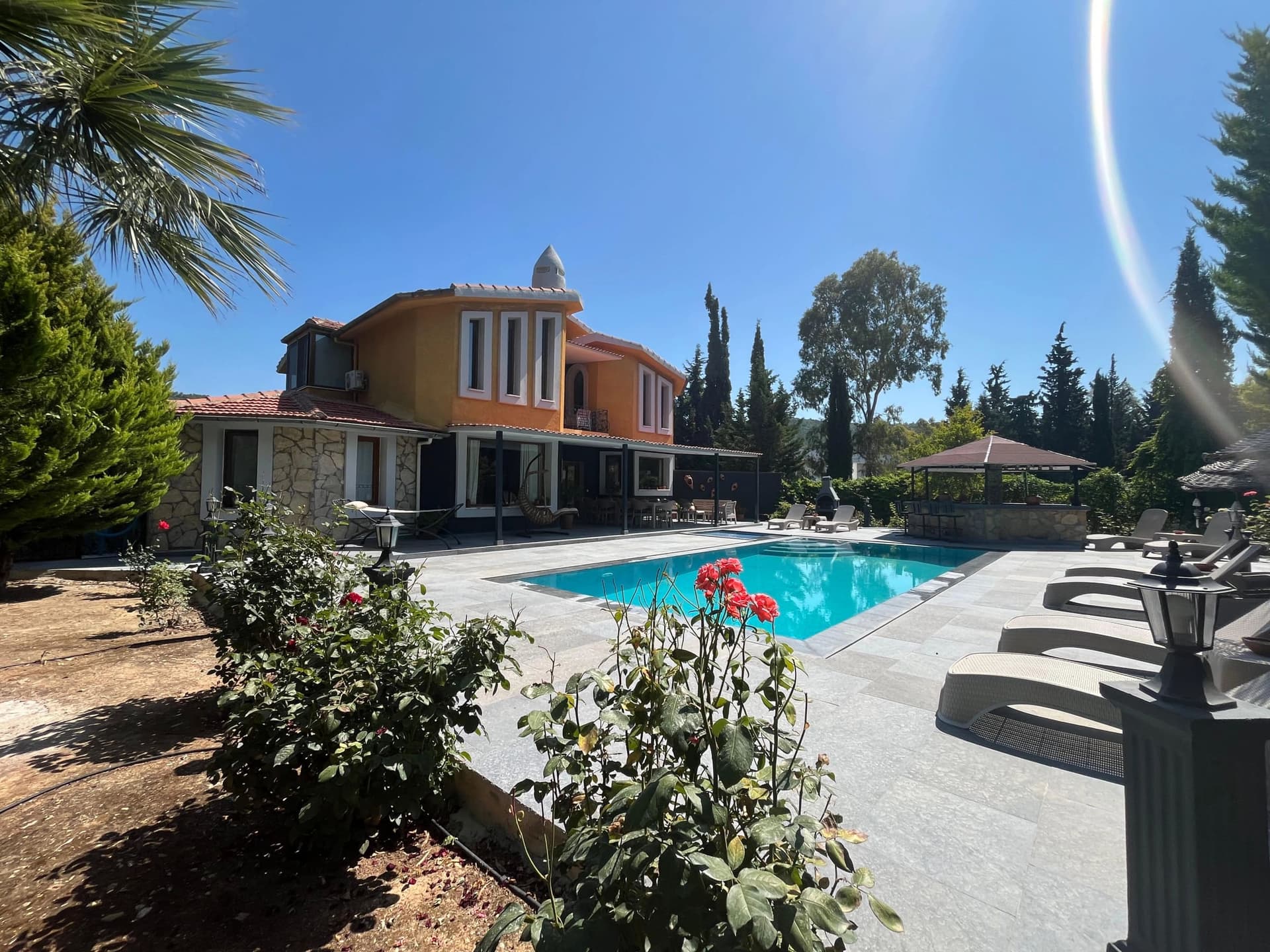 Bahçesinde yüzme havuzu ve şezlonglar bulunan sarı tonlu iki katlı müstakil villa.