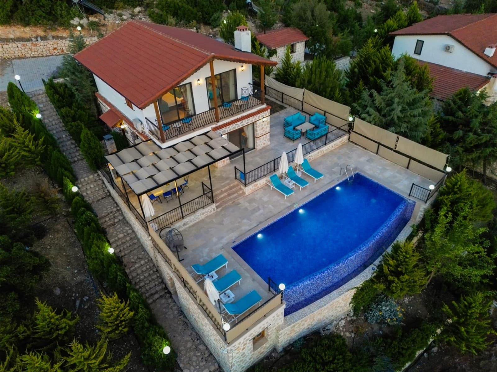 Kiremit çatılı taş villanın havuz ve bahçesinin havadan görünümü.