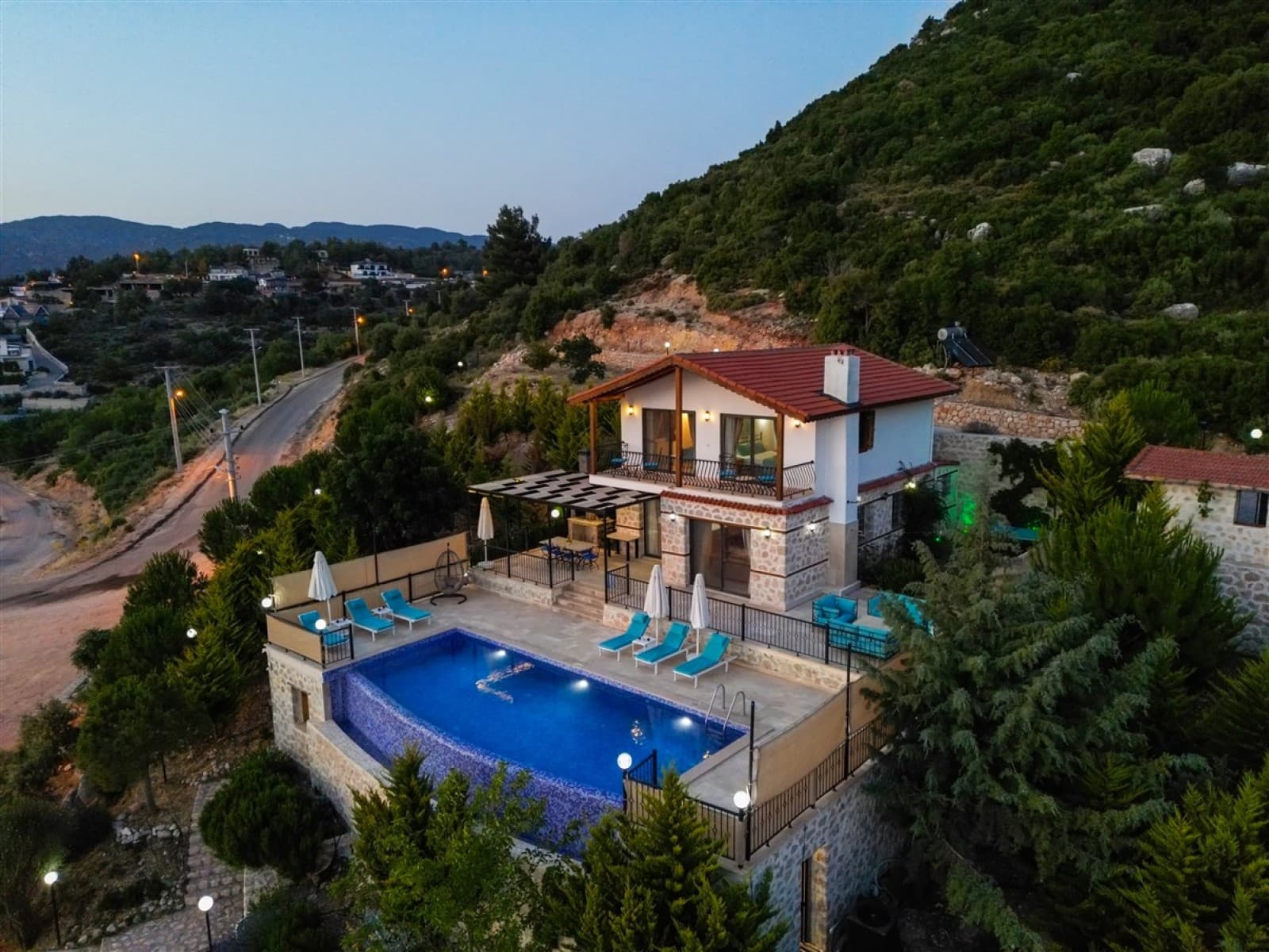 Bahçesinde havuz ve şezlonglar bulunan kiremit çatılı iki katlı taş villa.