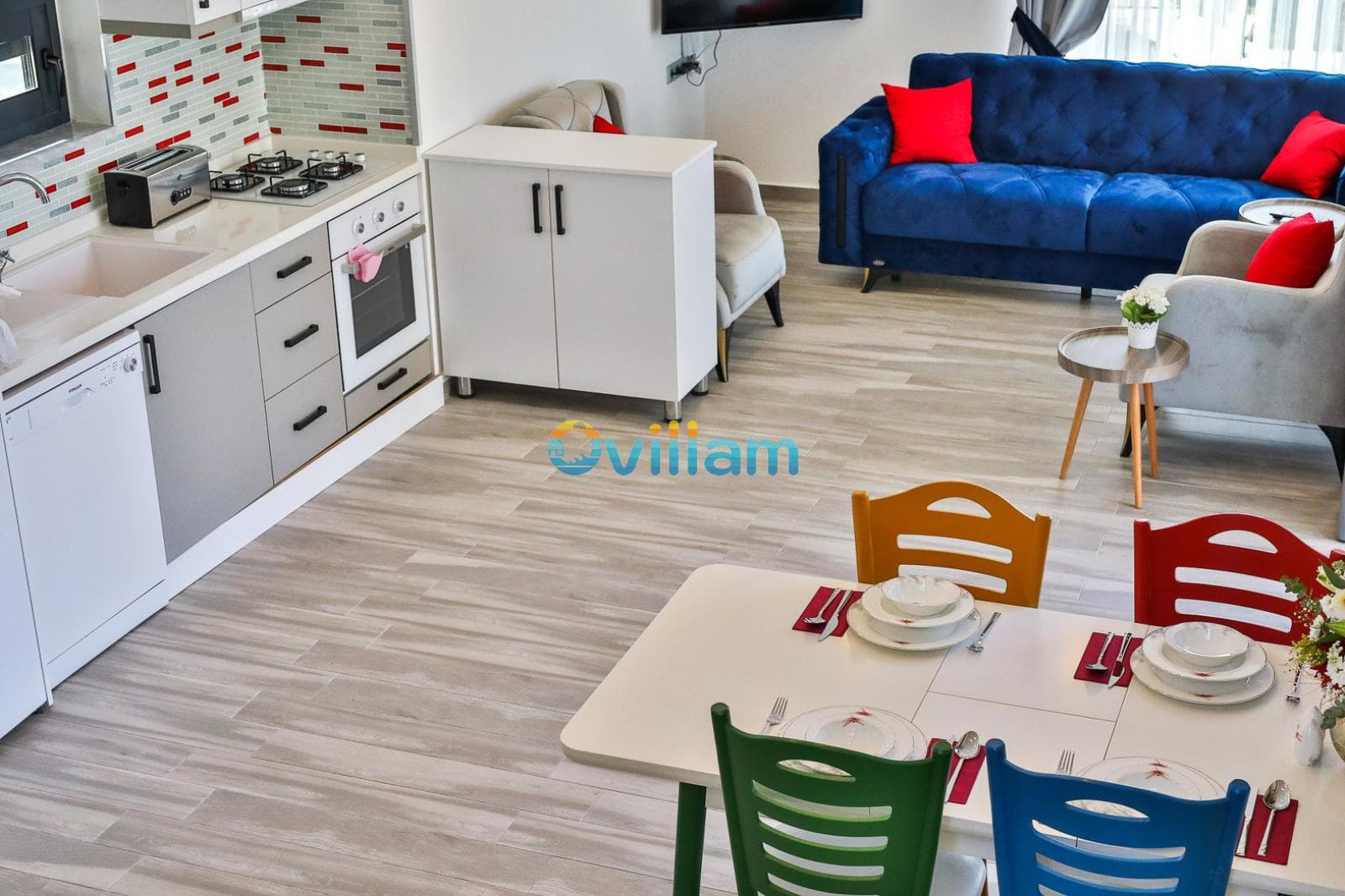 Açık mutfaklı oturma odası ve renkli sandalyeli yemek masası.