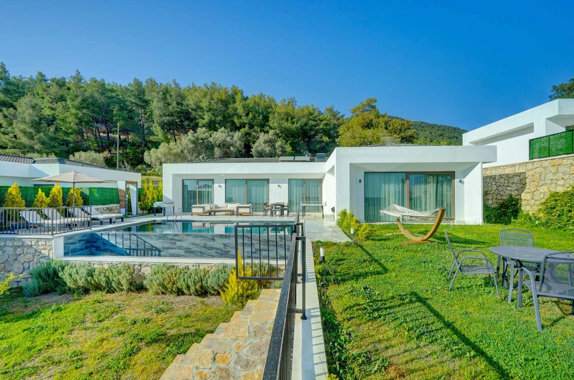 Bahçesinde havuz ve hamak bulunan beyaz tek katlı villa dış cephesi.