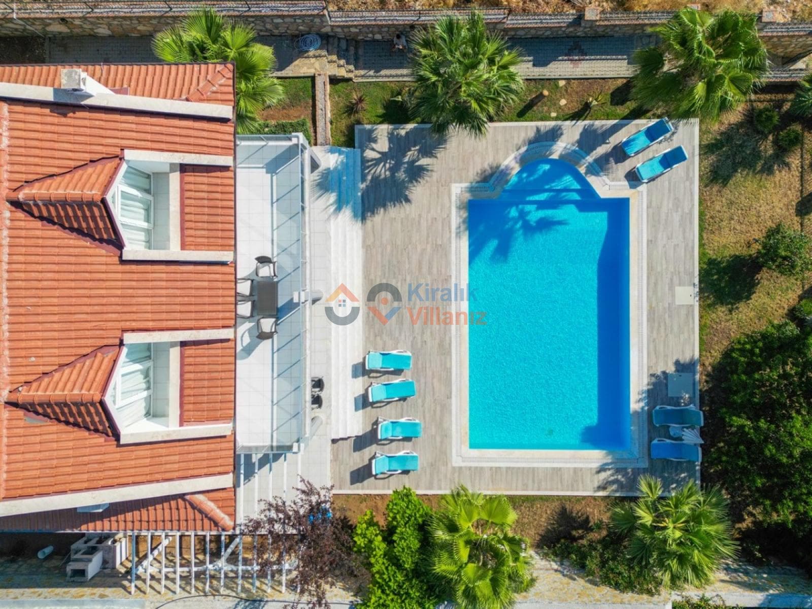 Havuz kenarında şezlonglar ve kiremit çatılı villanın havadan görünümü.