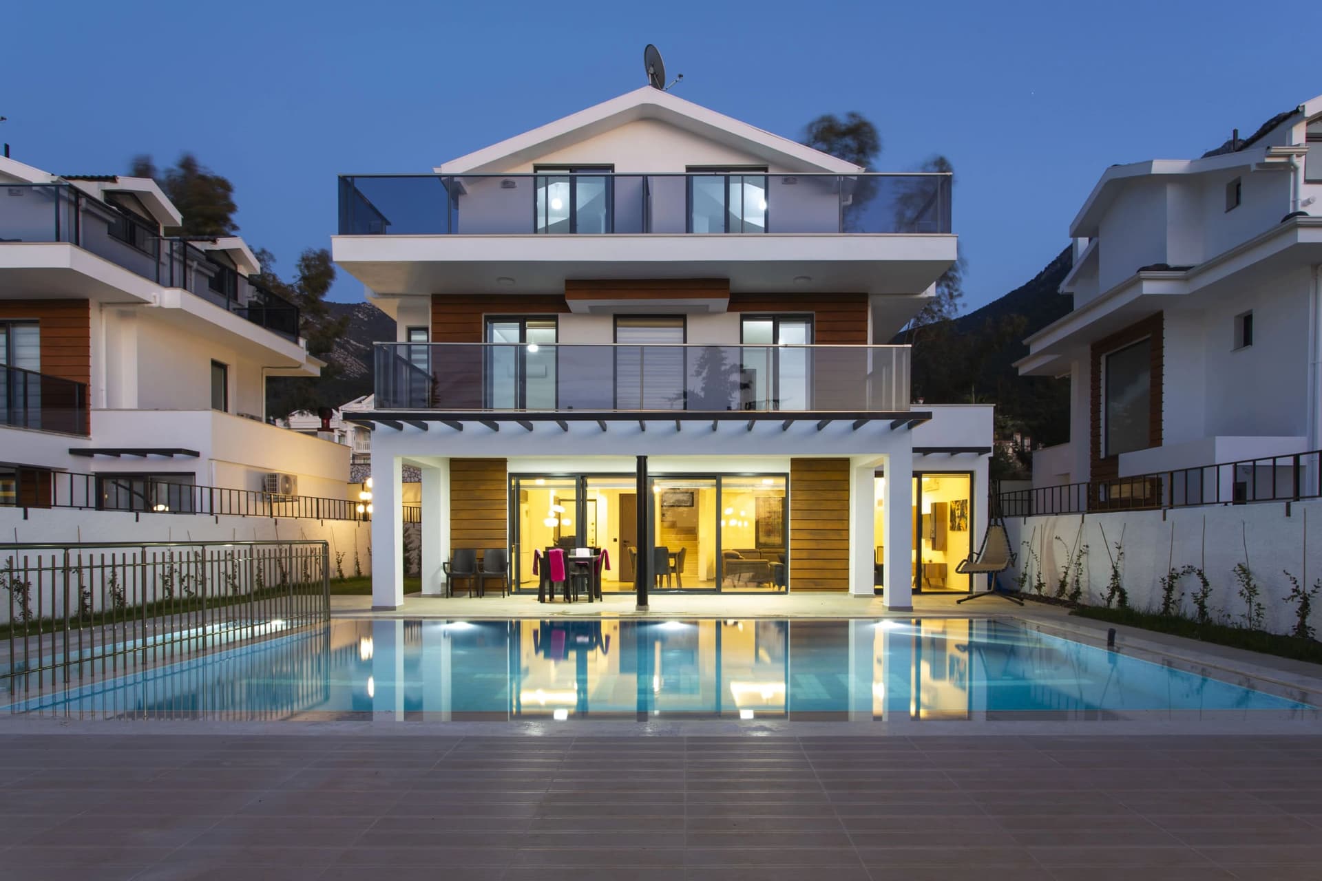 Akşam ışıklandırılmış modern villanın havuzlu dış cephesi.
