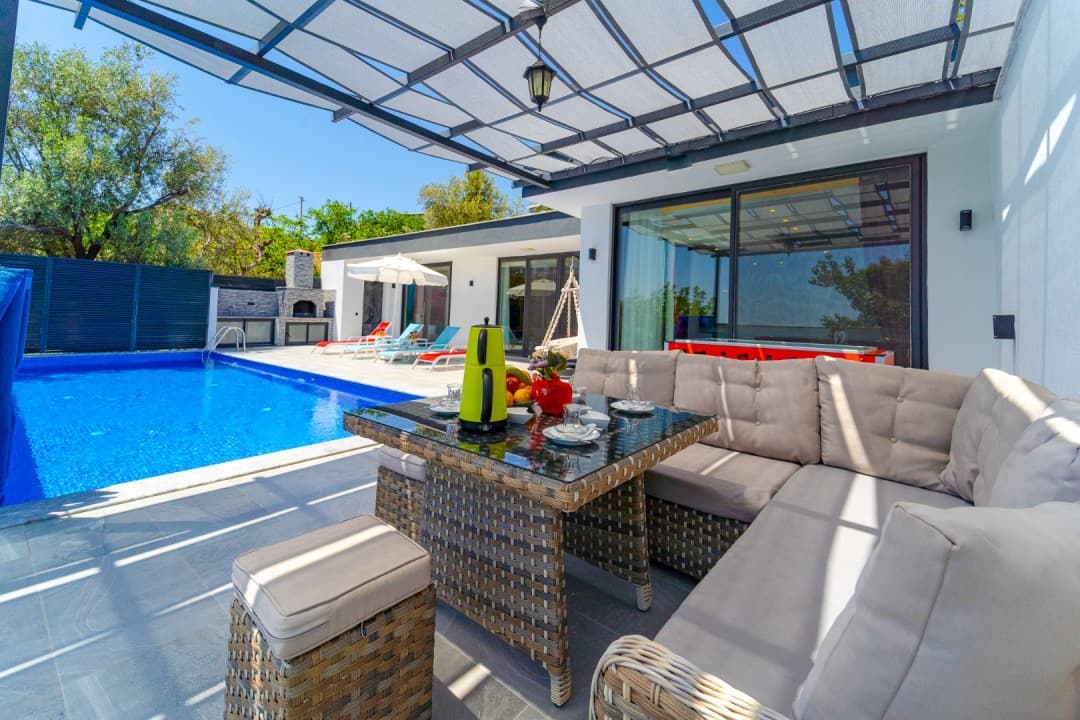 Veranda kısmında hasır oturma grubu, yemek masası ve yanında özel yüzme havuzu bulunan modern villa.