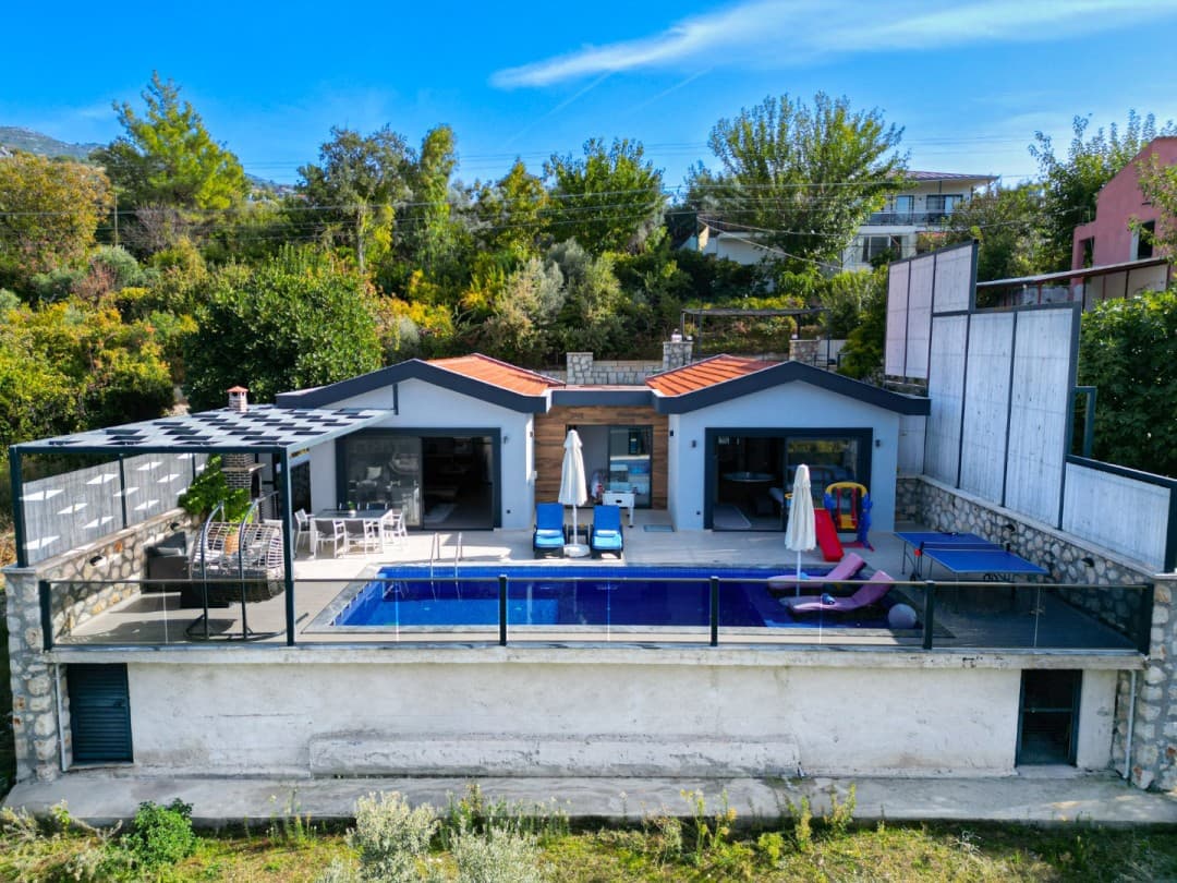 Önünde yüzme havuzu, şezlonglar, masa tenisi ve oturma grubu bulunan tek katlı müstakil villa.
