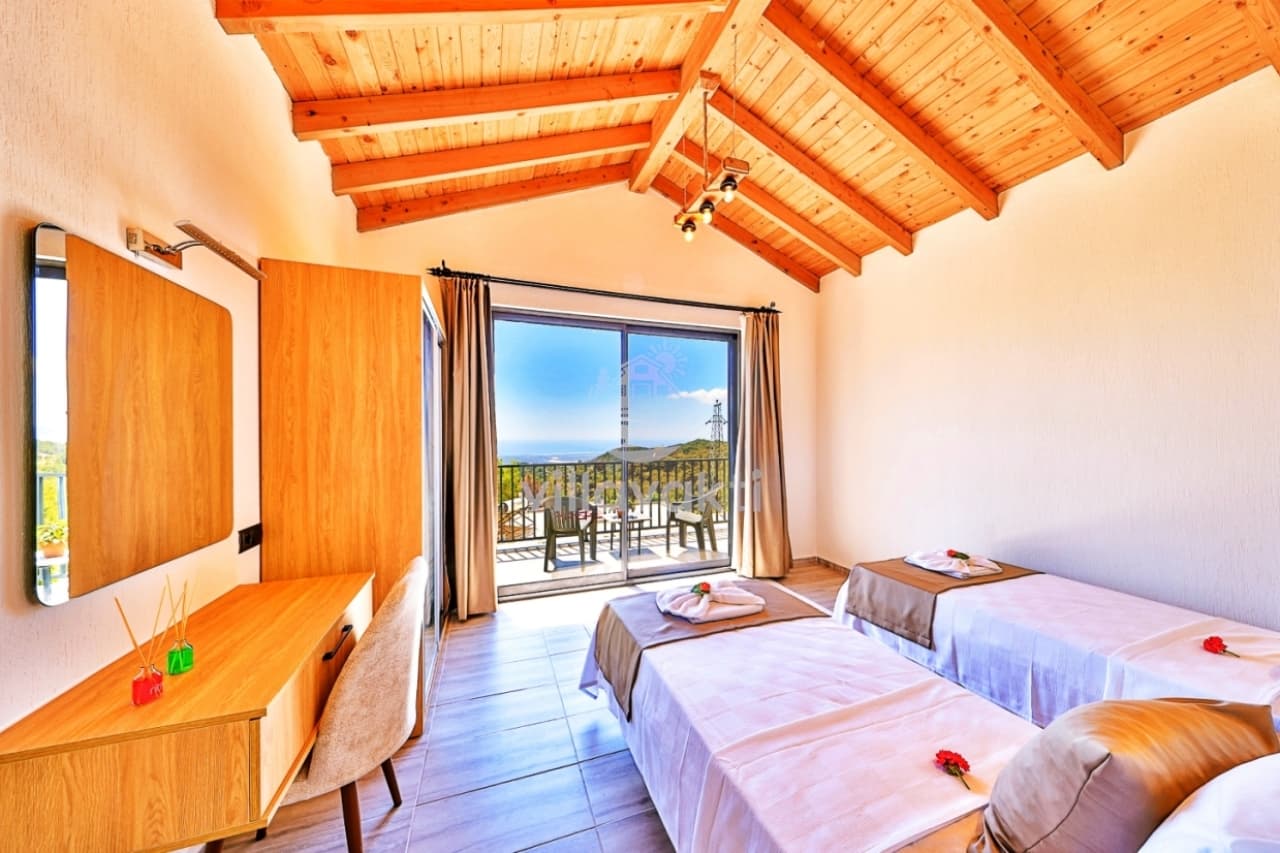 Ahşap tavanlı yatak odasında iki tek kişilik yatak ve manzaralı balkon bulunuyor.
