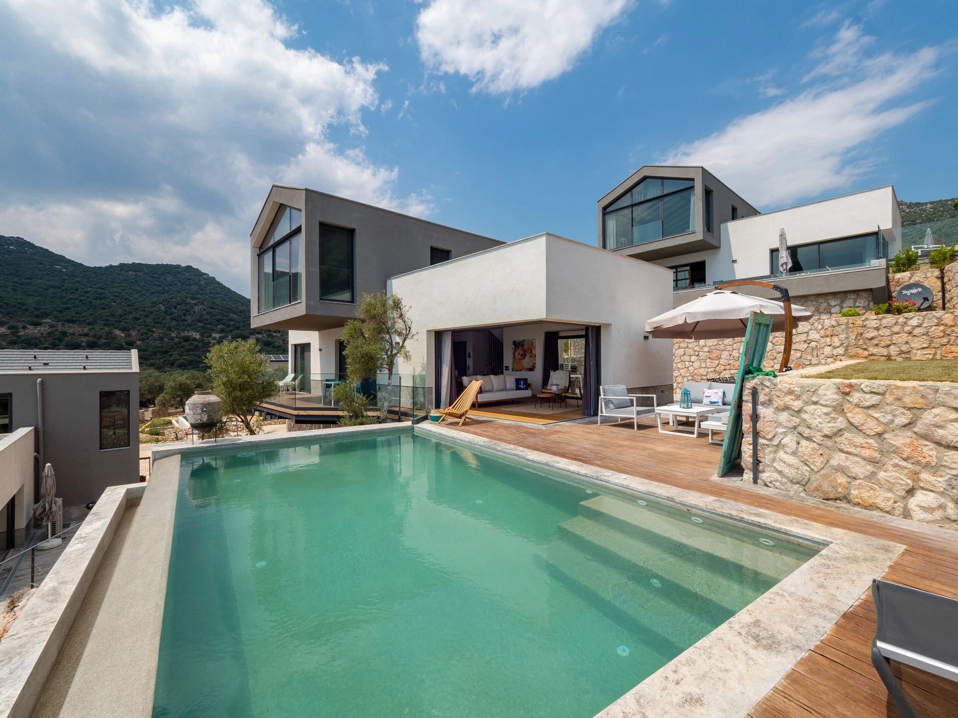 Geniş havuzlu ve dağ manzaralı modern villa dış cephesi.