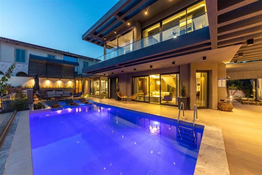 Akşam saatlerinde aydınlatılmış modern villanın havuzu ve şezlongları.