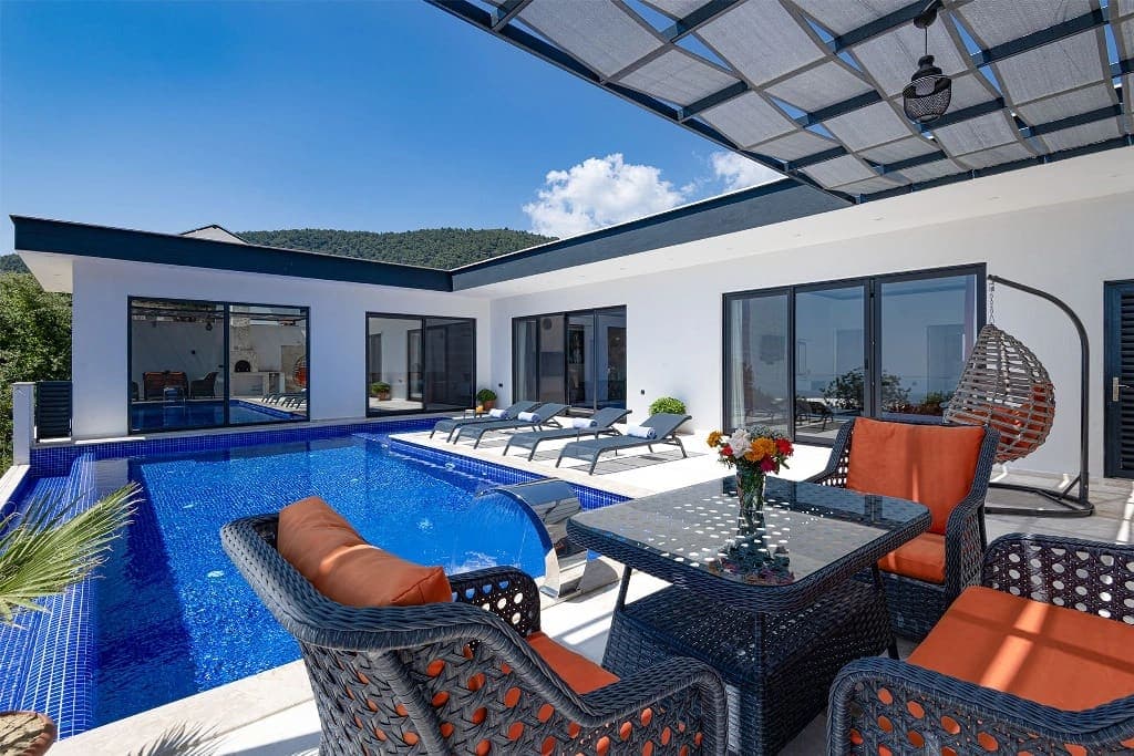 Terası, havuzu ve turuncu minderli oturma grubu olan villa dış mekanı.