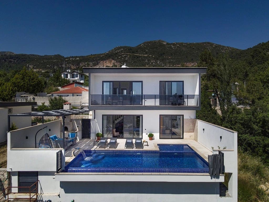 İki katlı modern villanın önünde mavi havuz ve dağ manzarası var.