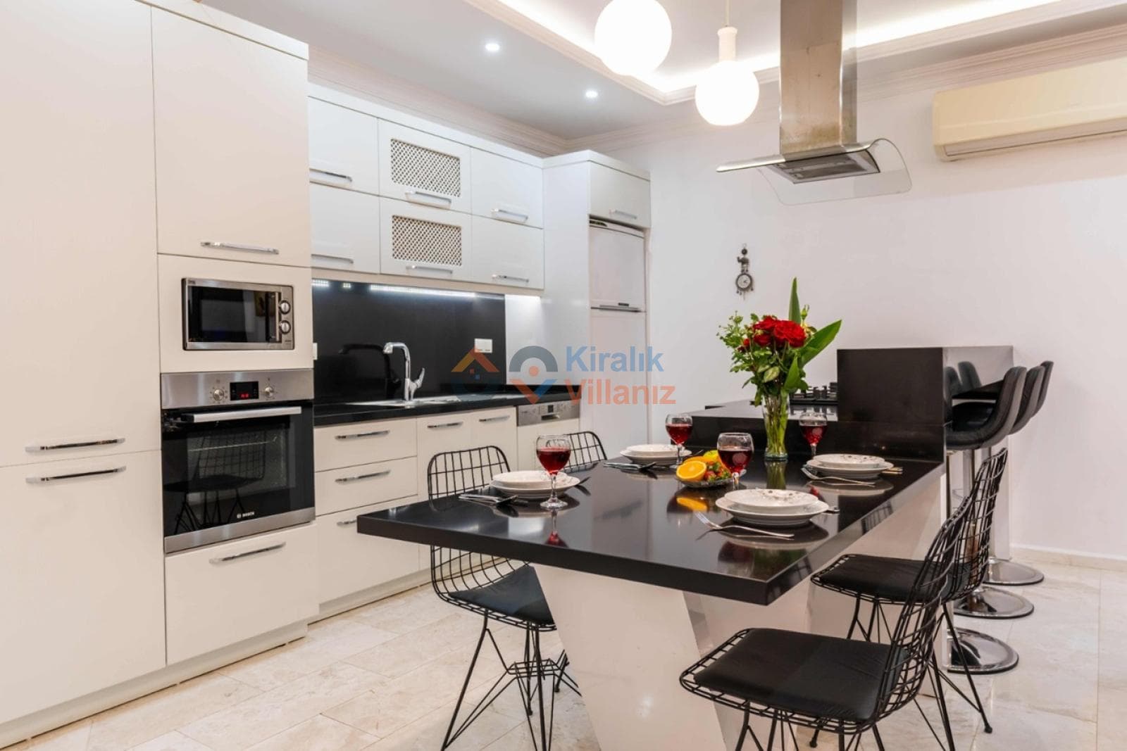 Beyaz ve siyah dolaplı modern mutfakta yemek masası bulunuyor.