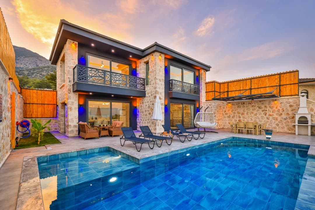 Akşam karanlığında havuzu ve şezlongları bulunan iki katlı taş villa.